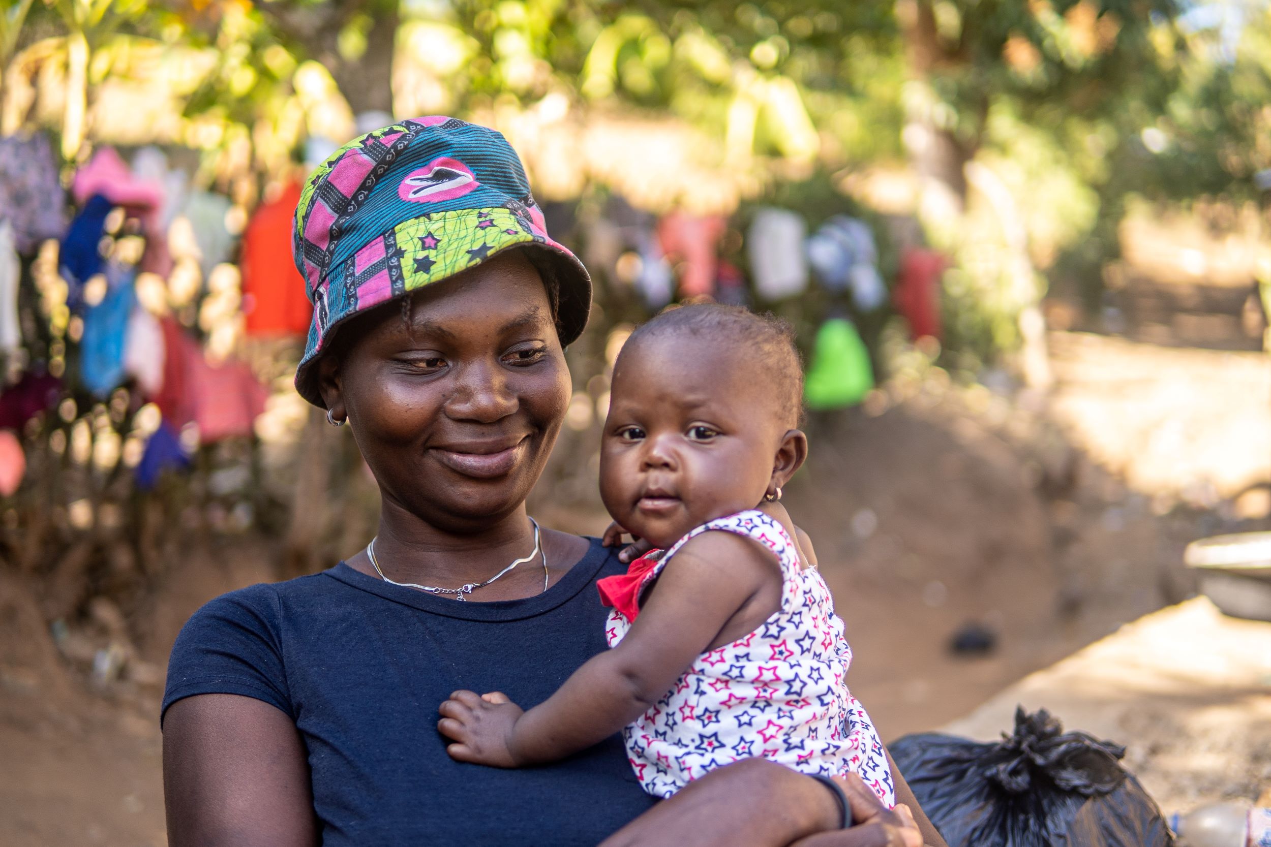 Haitian woman in blue t-shirt and hat smiling with baby girl in arms