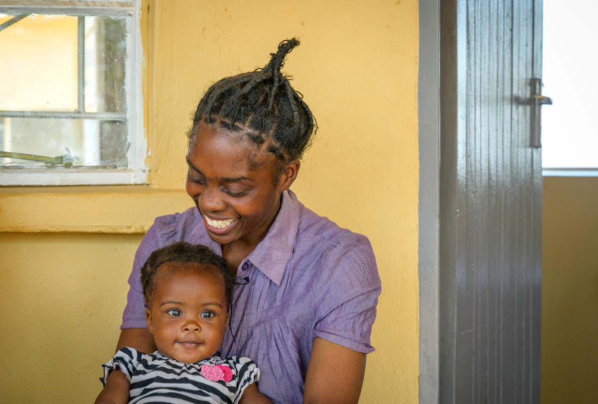 Zambian mother and baby daughter sat together smiling outside a health clinic