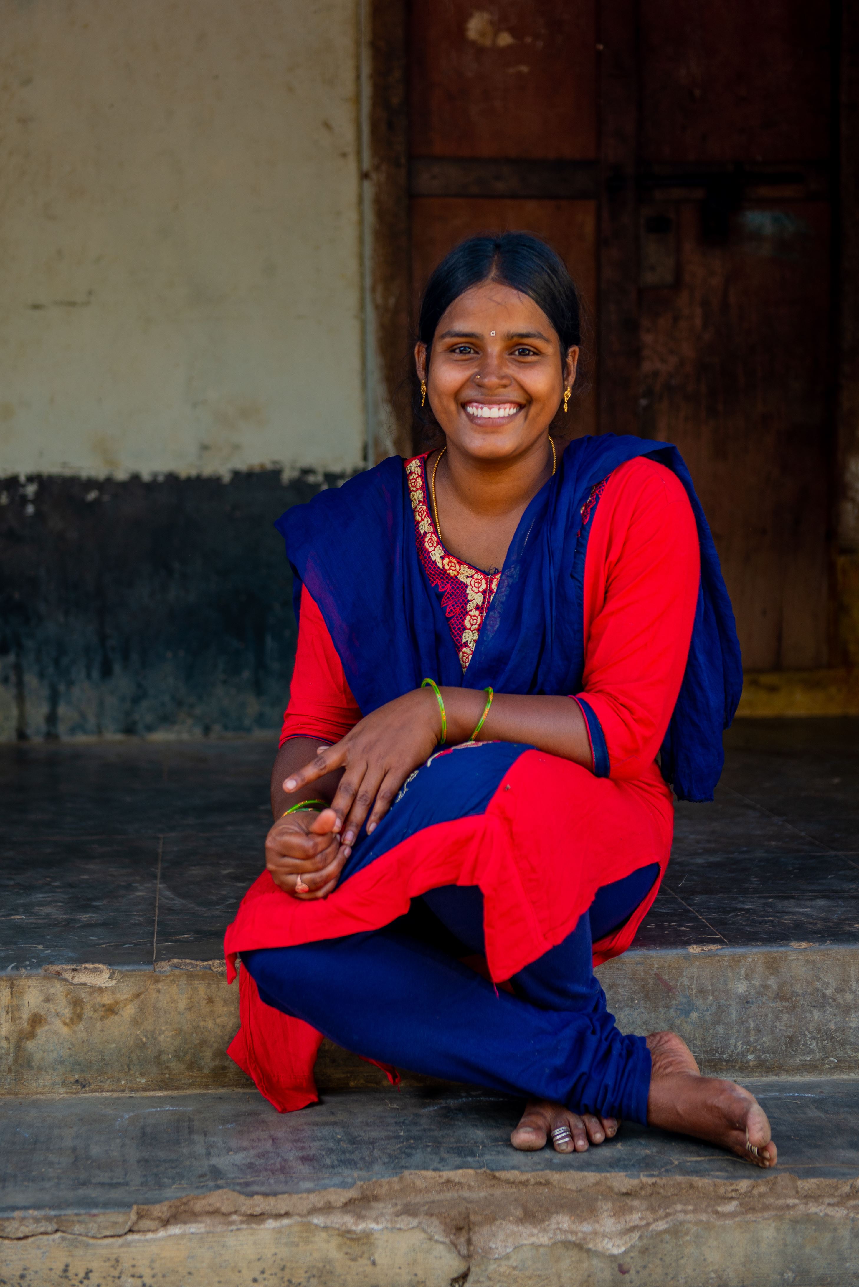 Girl in India sits outside her home, smiling as she talks about helping prevent child marriages for others