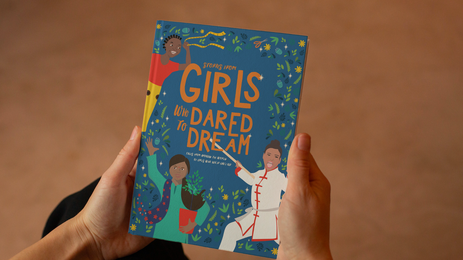 Hands hold a hardcover version of the book 'Stories from girls who dared to dream', with bright, bold illustrated cover