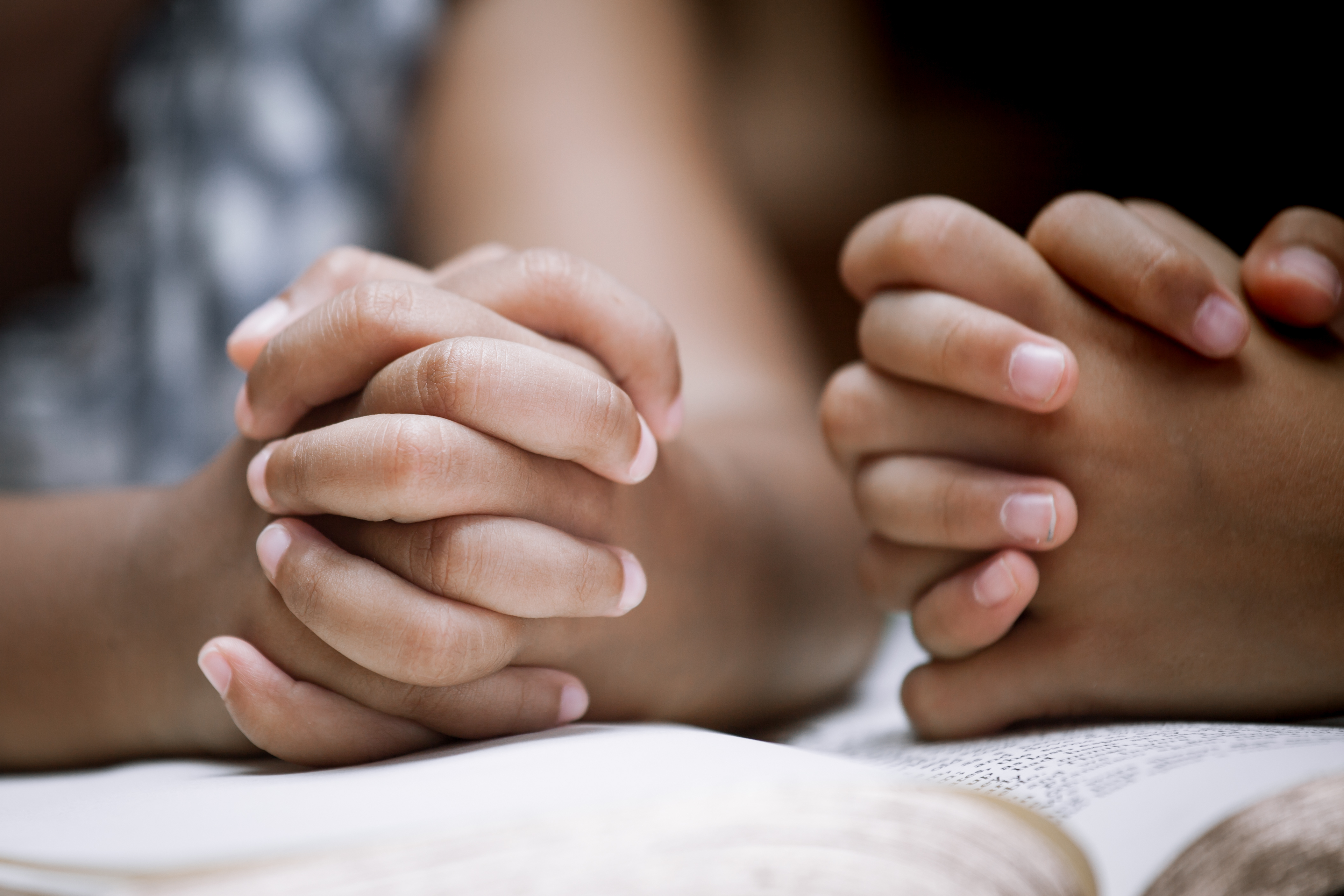 Two children’s hands clasped in prayer over a book