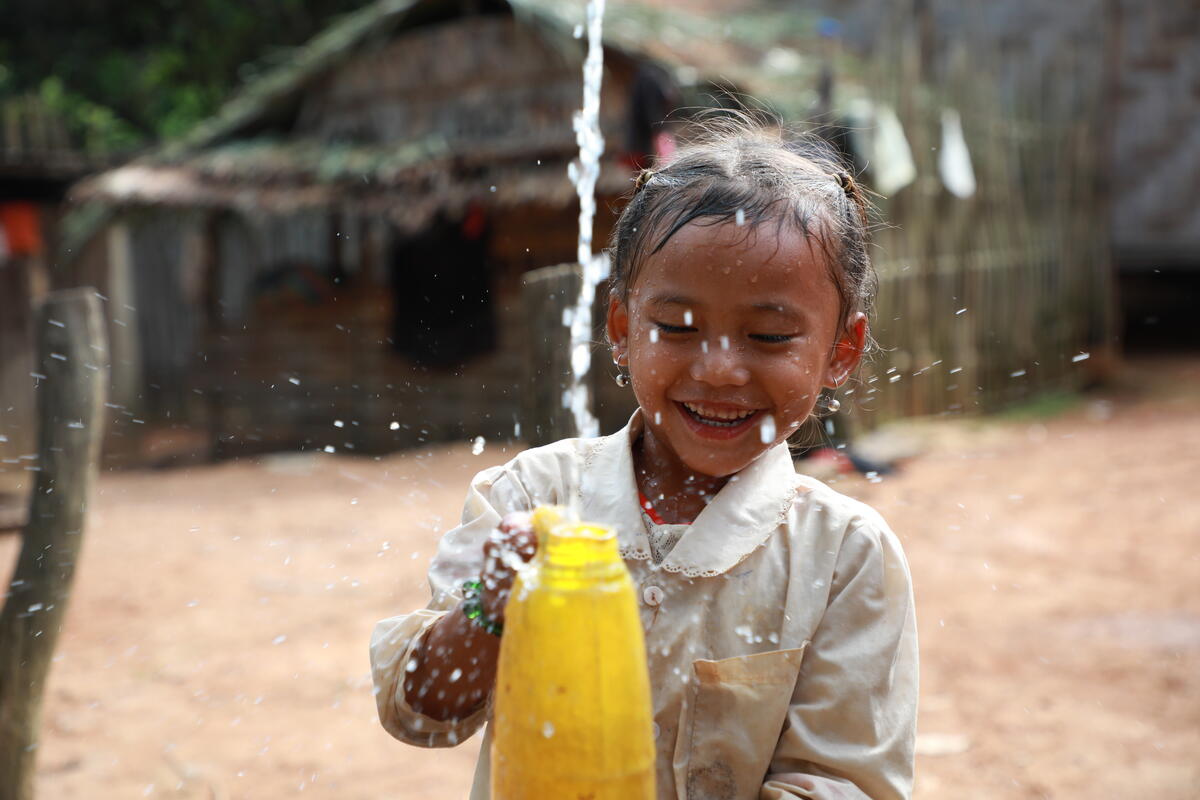 A young child in Laos smiles whist collecting fresh, running water.