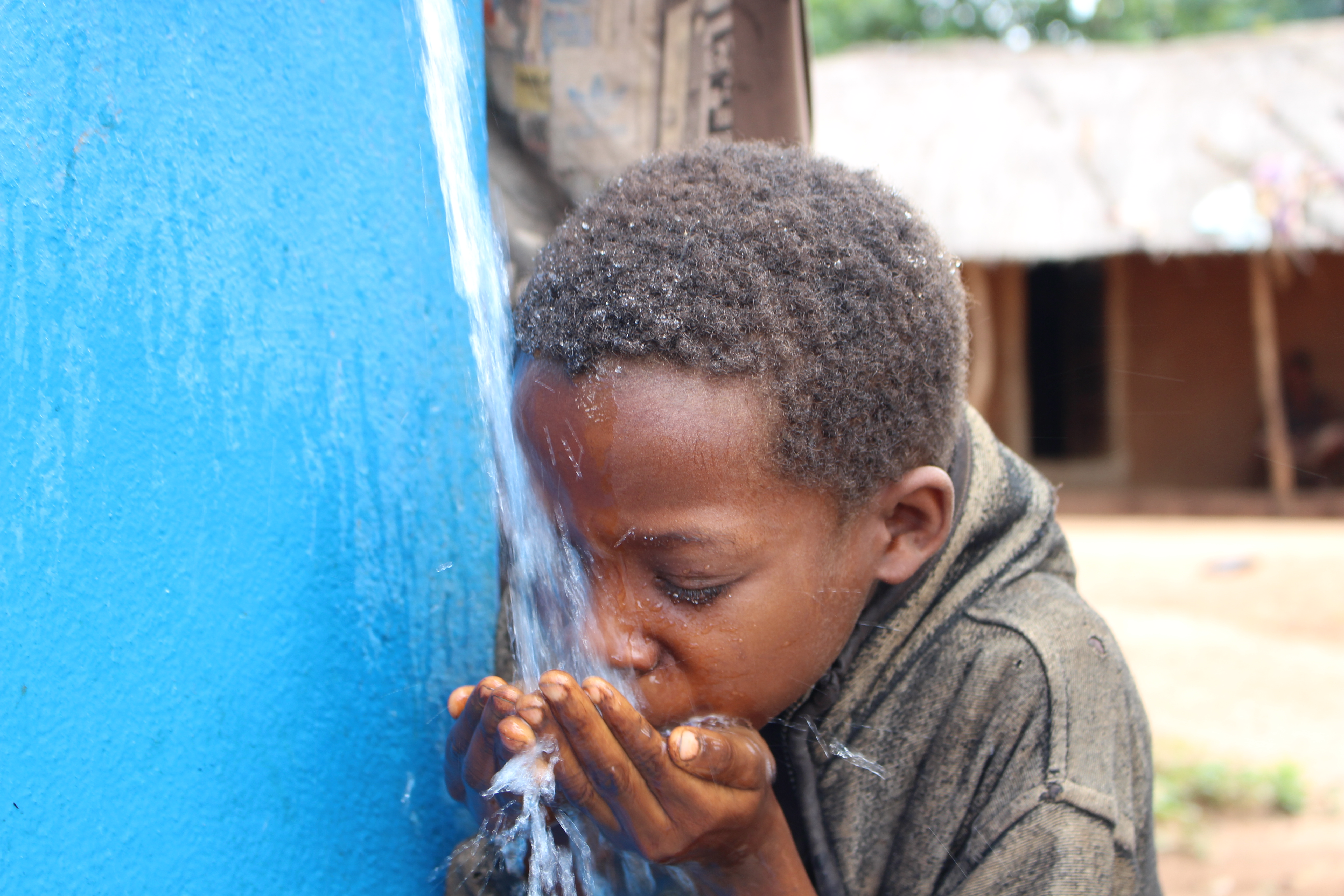 A young boy drinks water from an outdoor clean water tap