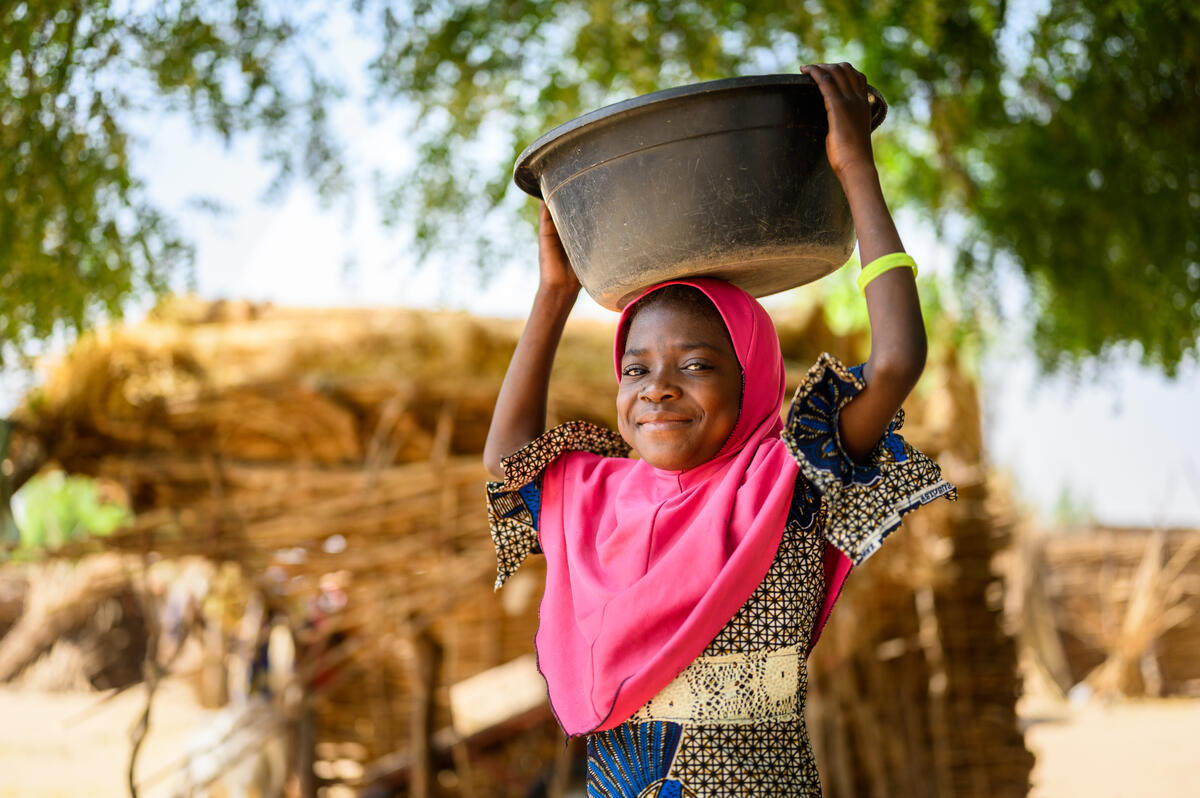 Girl from Niger smiles while holding a water bucket on her head