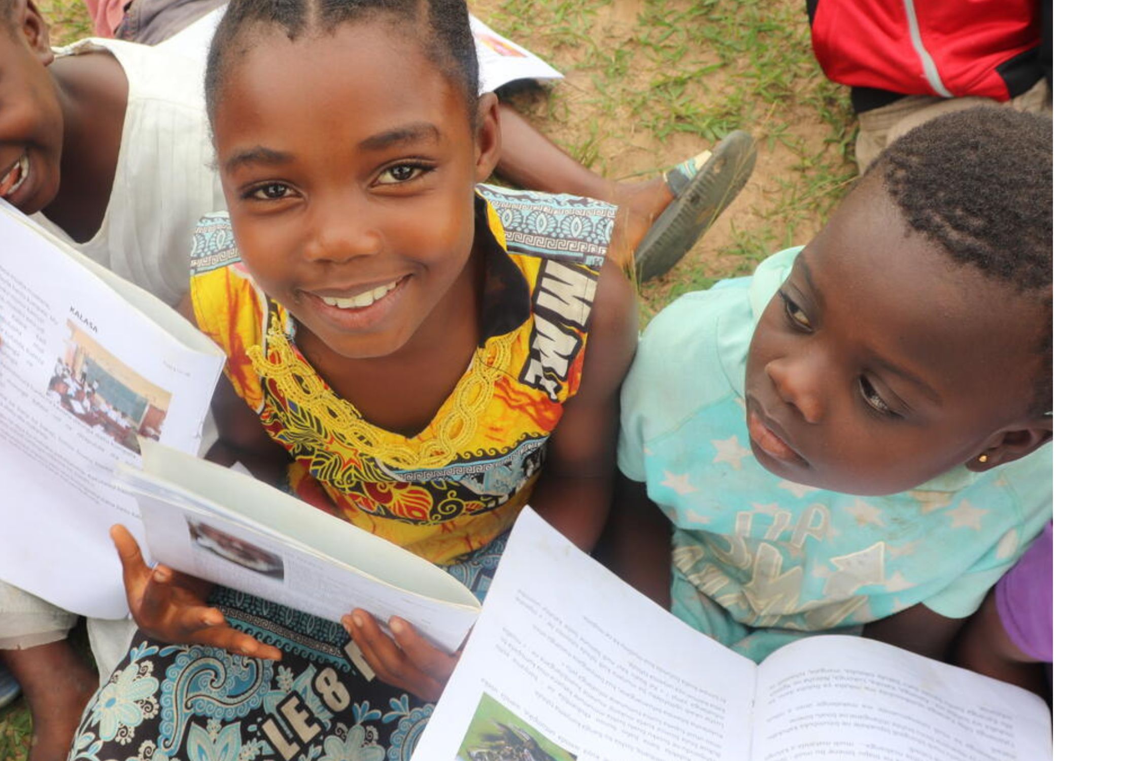 Girl from DRC smiling and holding a reading book amongst other school children