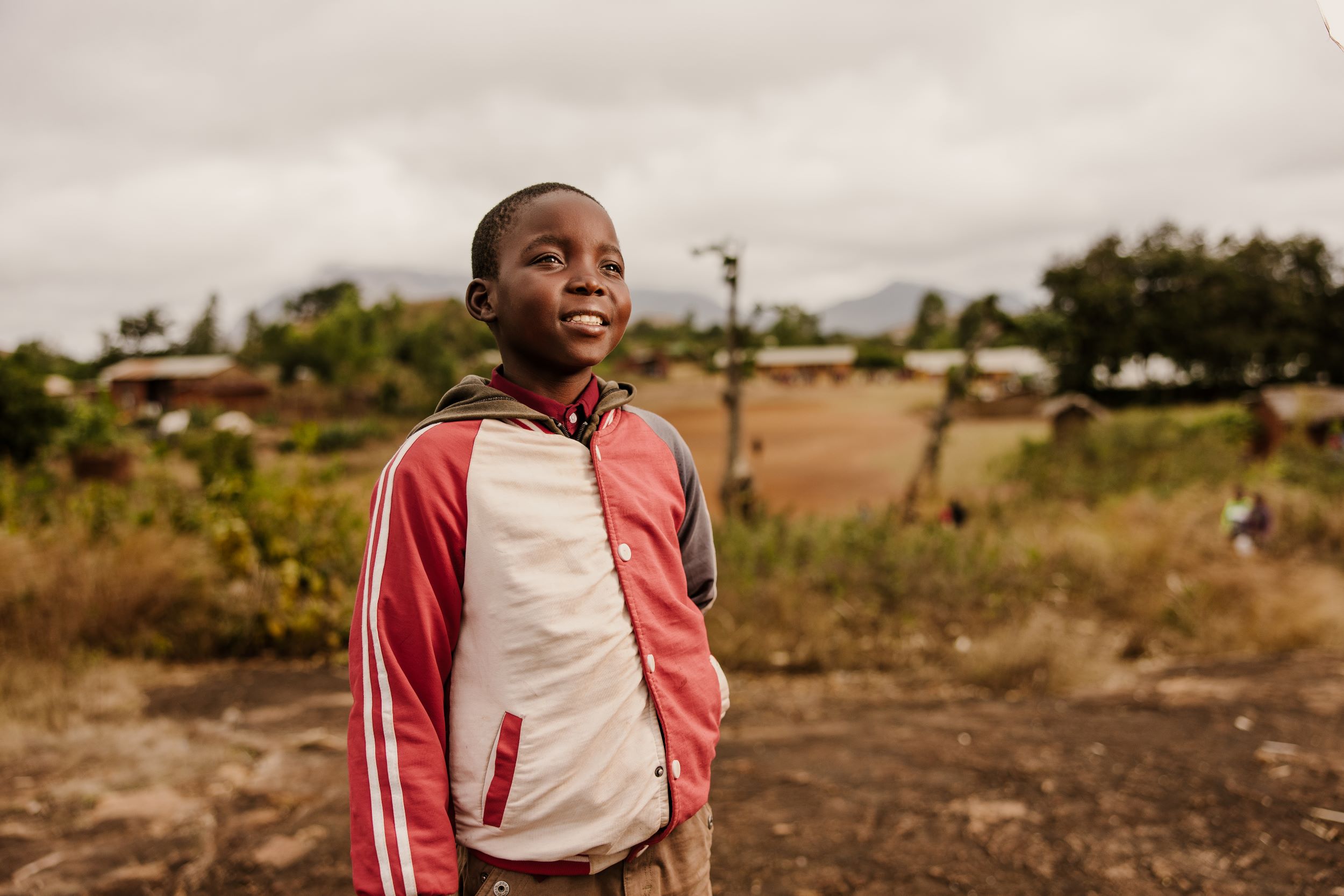 Boy from Malawi smiling in red and white jacket