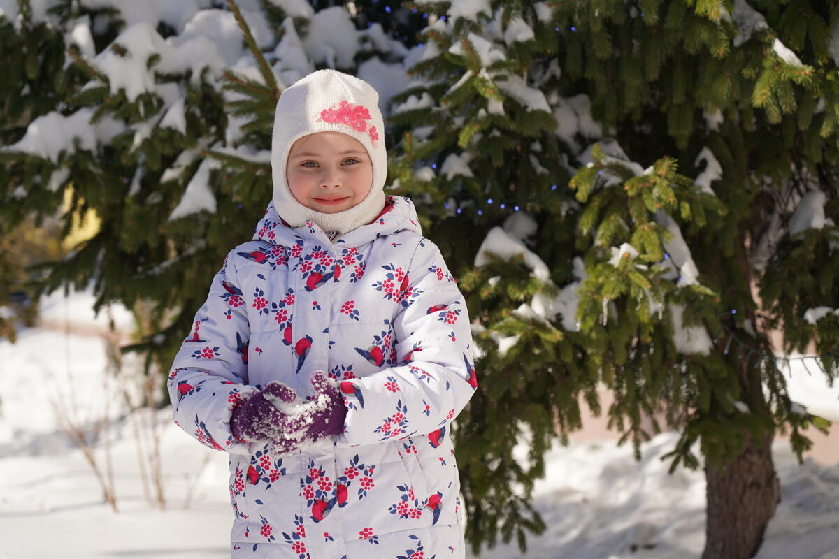 A young girl from Ukraine wrapped up in warm clothes stands among the snow