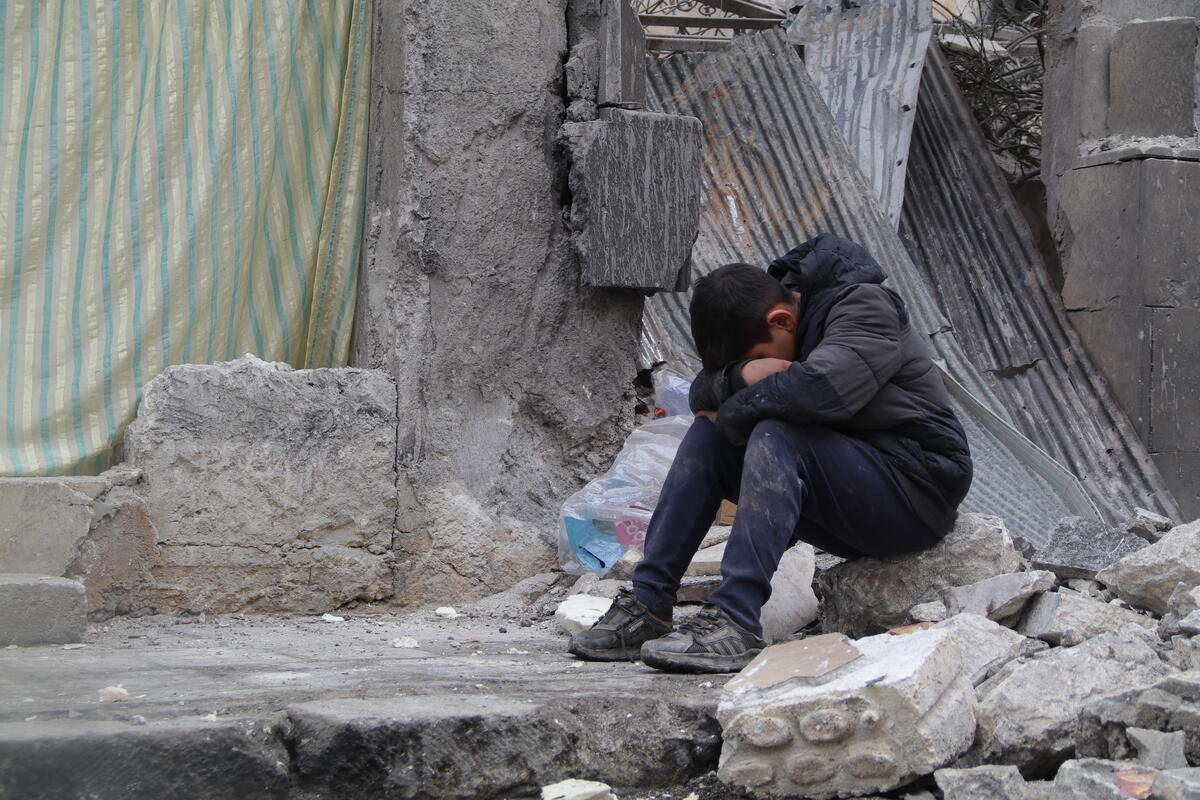 Child sits in rubble with his head bowed to his knees