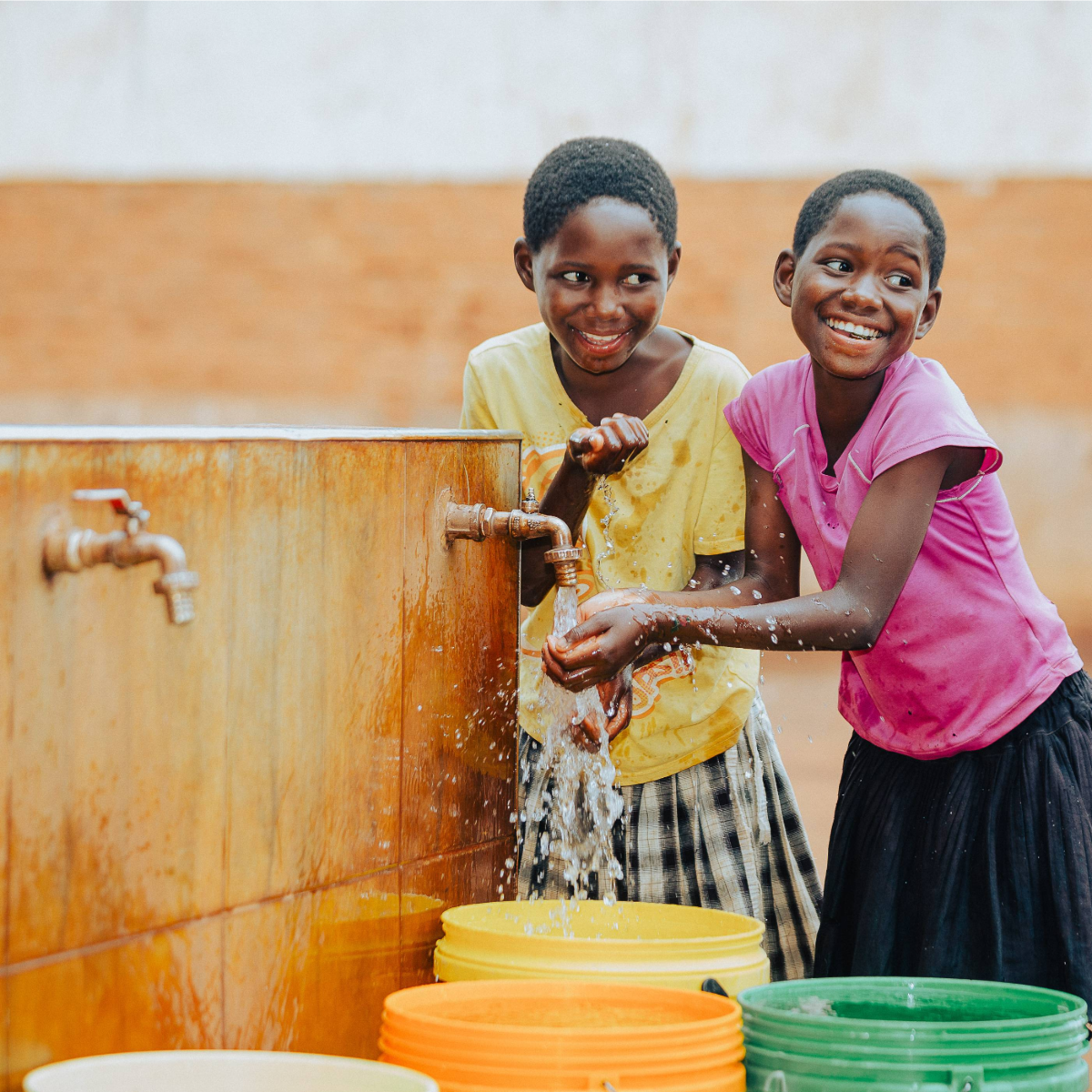 Two girls wash their hands at a community water point in Malawi with clean water flowing from a tap.
