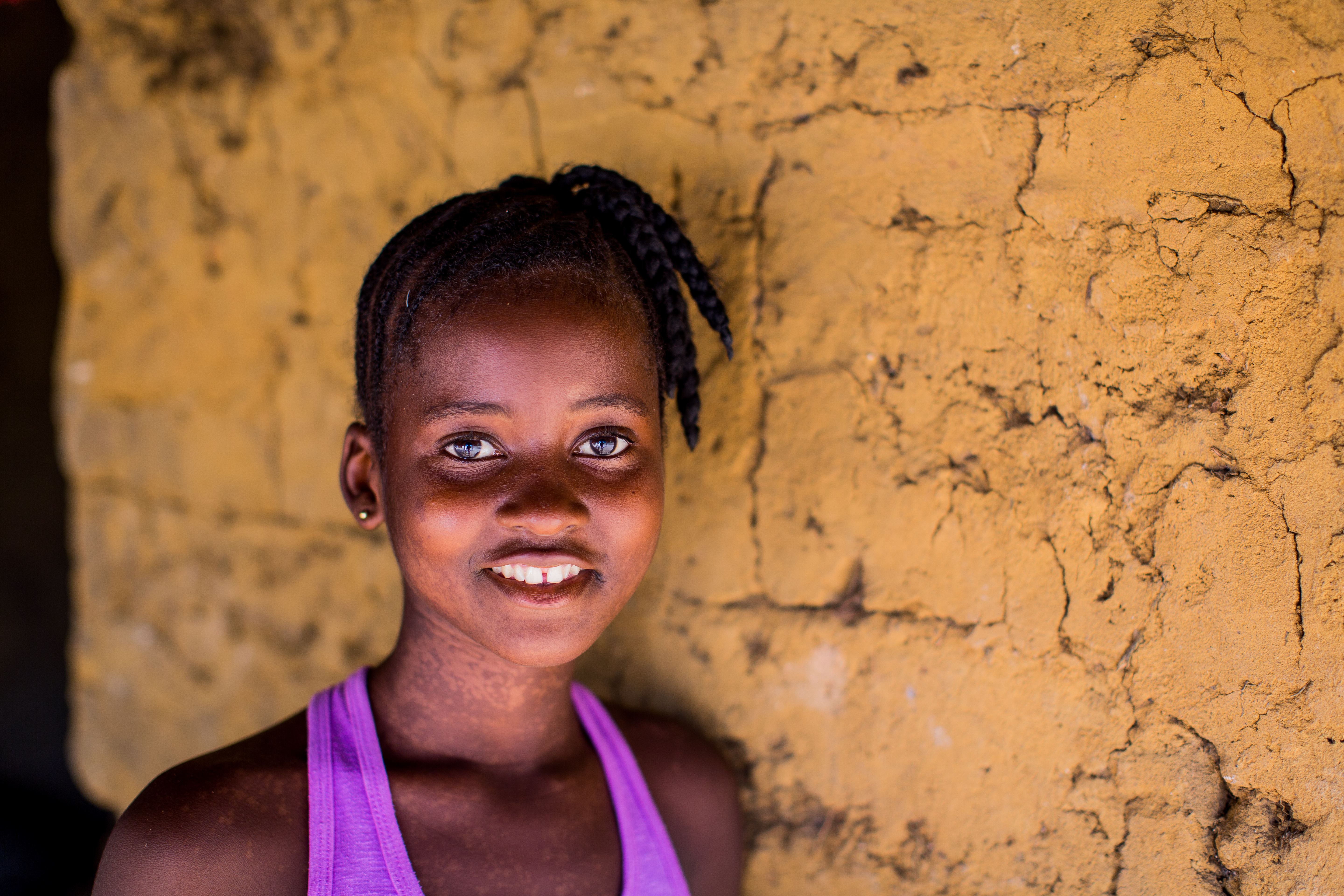 Sponsored girl in Sierra Leone smiles as she stands against a yellow wall