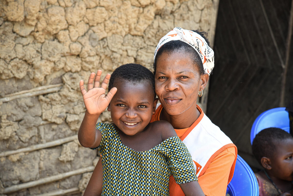 A young girl in DRC waves at the camera while sitting on a WV staff's lap