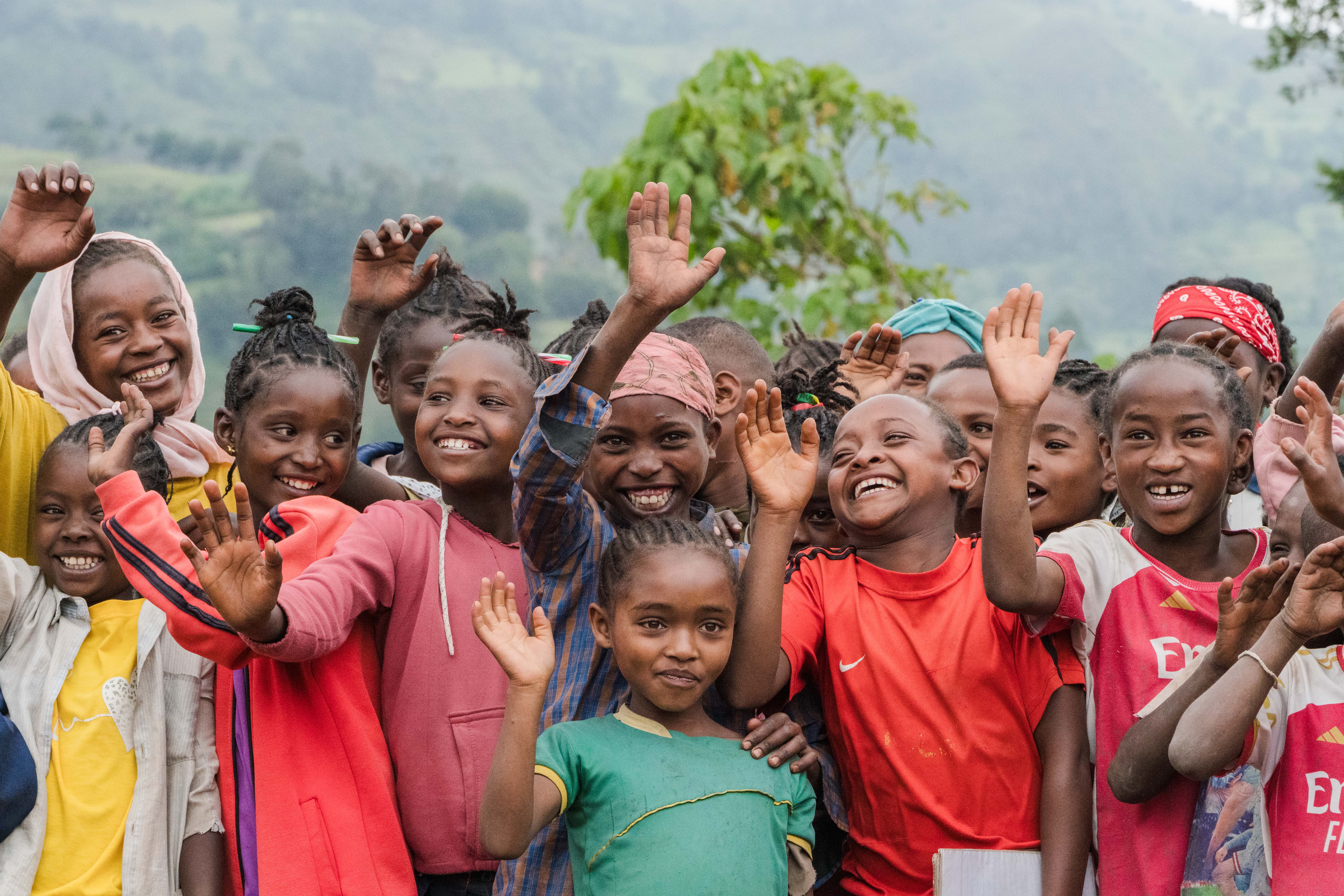 Large group of young children smiling and waving their hands in the air.