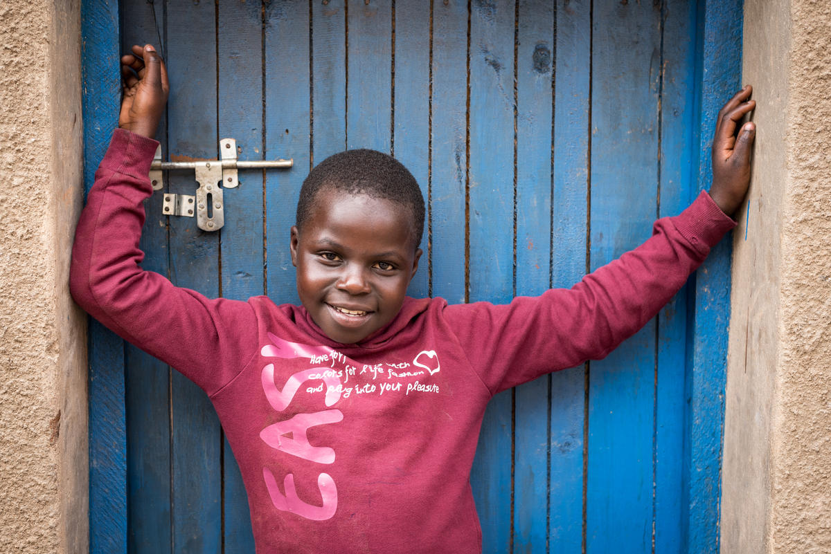 Child smiles in front of a blue door at her home in Rwanda