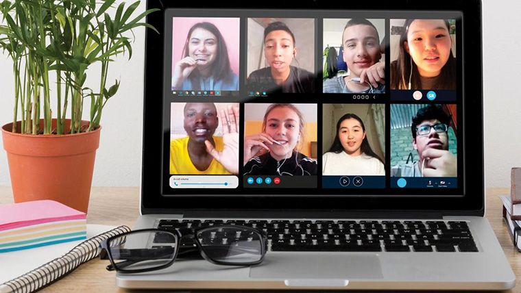 8 children talk over Zoom on a laptop, next to a potted plant