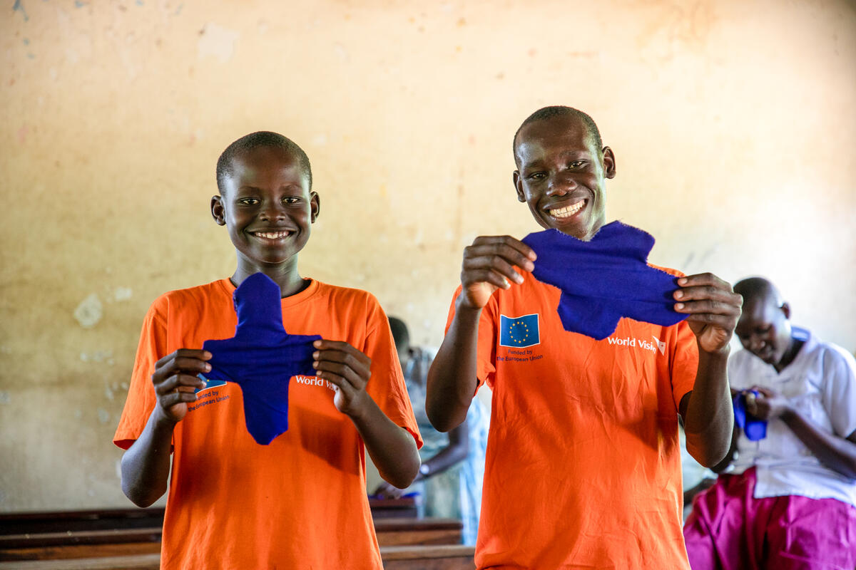 Two Ugandan school boys smiling and holding up handmade sanitary pads