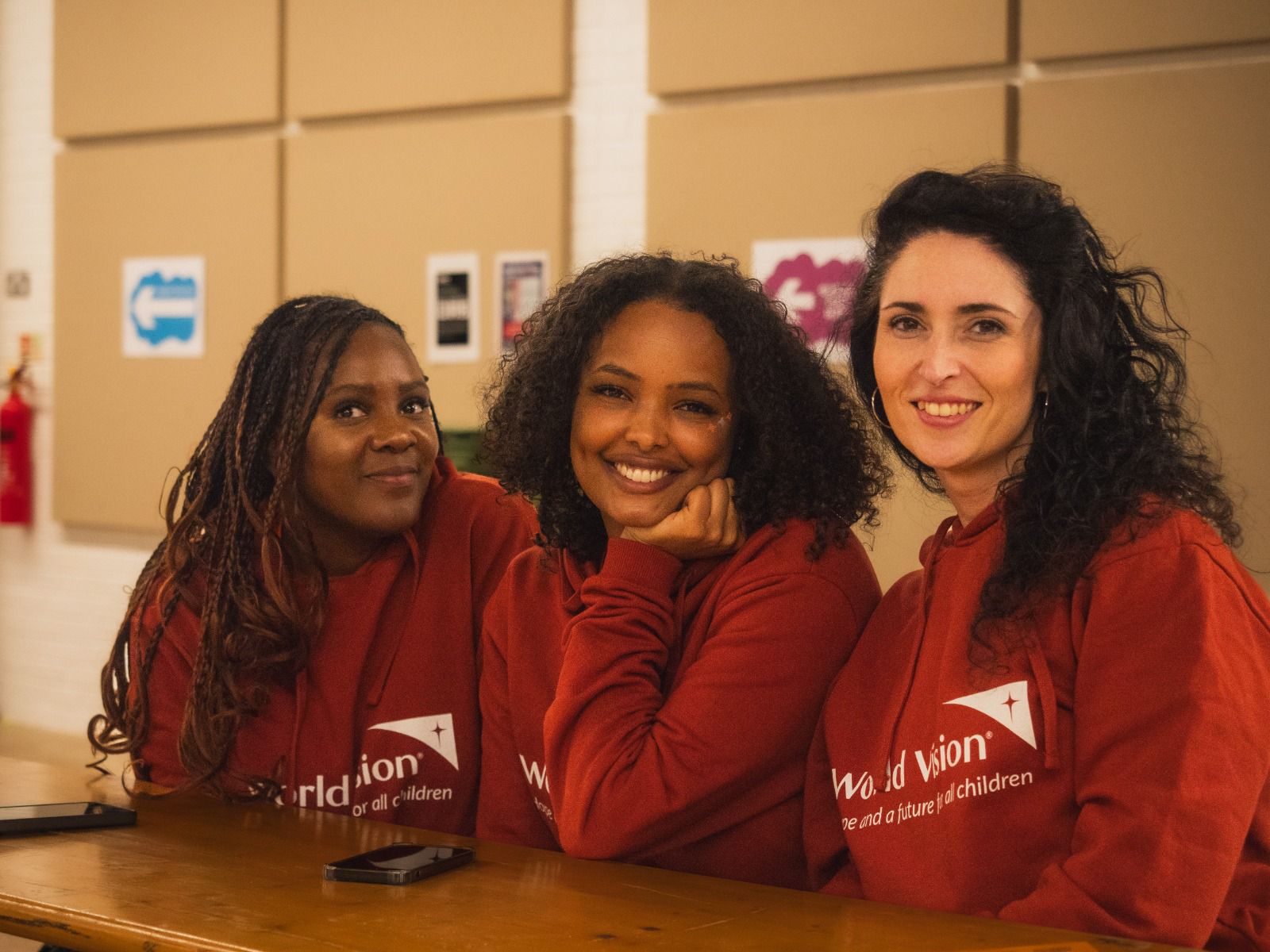 Three women sitting smiling at festival wearing World Vision hoodies