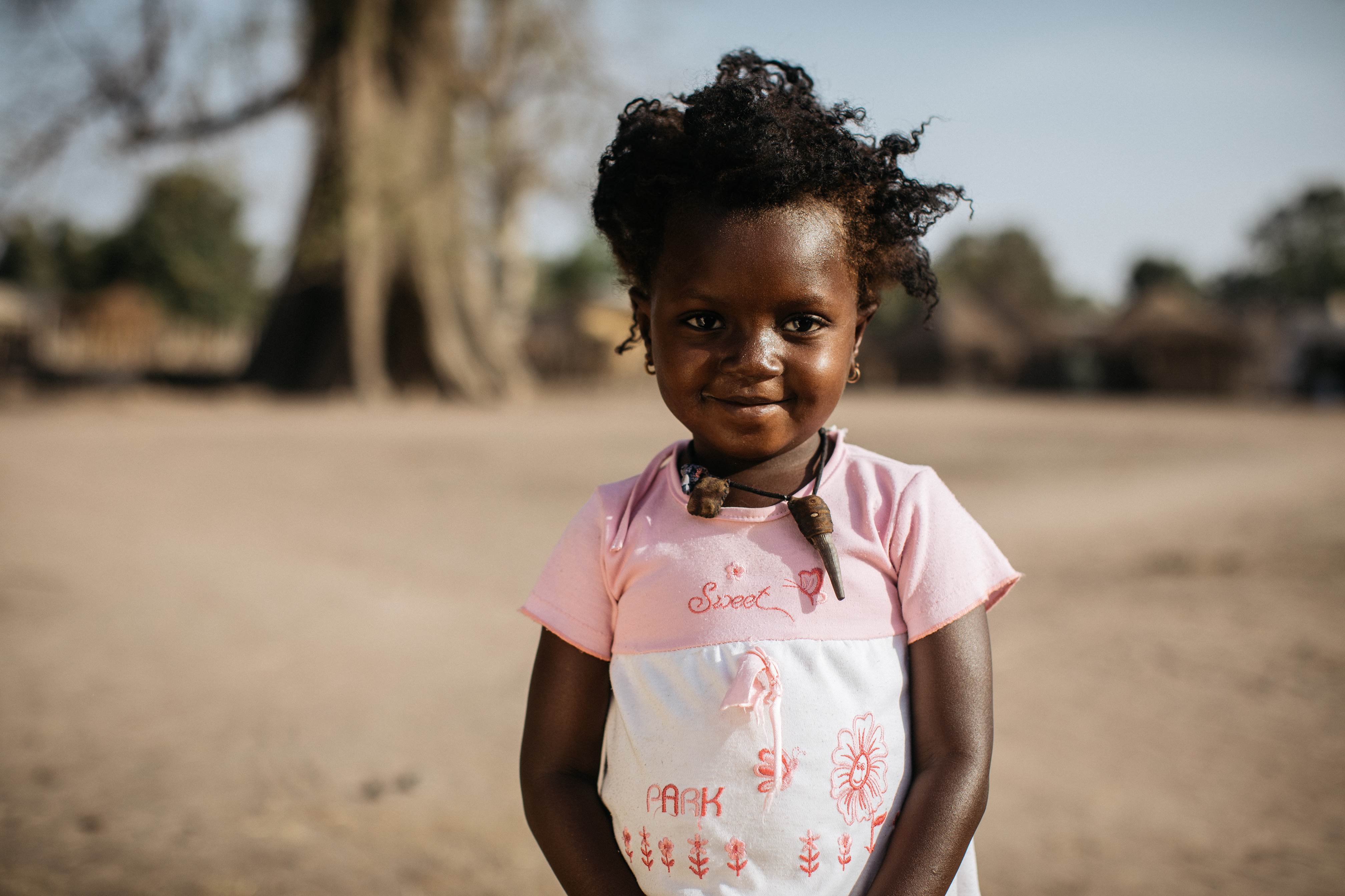 3 year old girl from Senegal smiles to the camera wearing a pink and white top