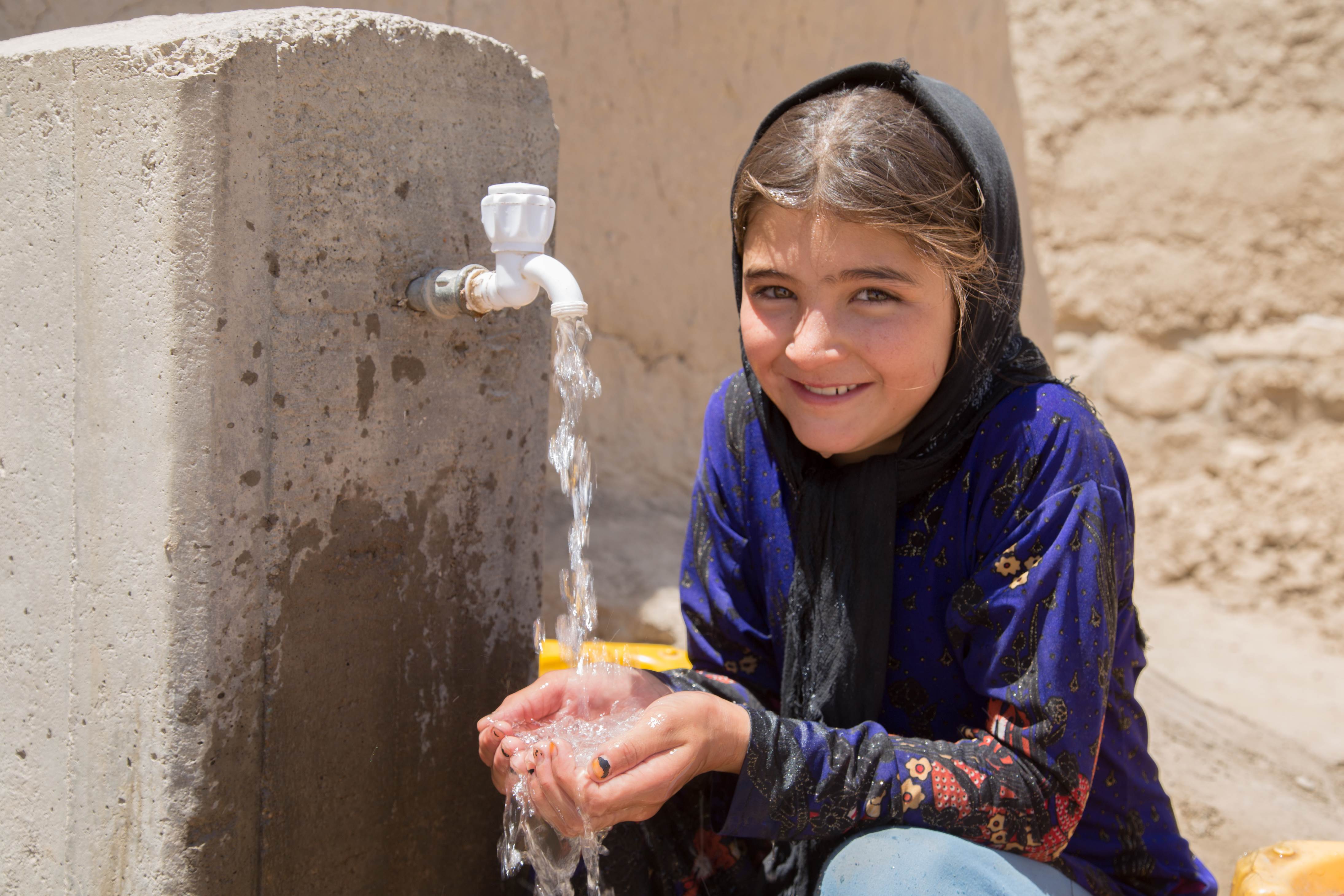 Afghan girl smiles as she washes her hands in clean water from a World Vision established solar-powered, filtered water source