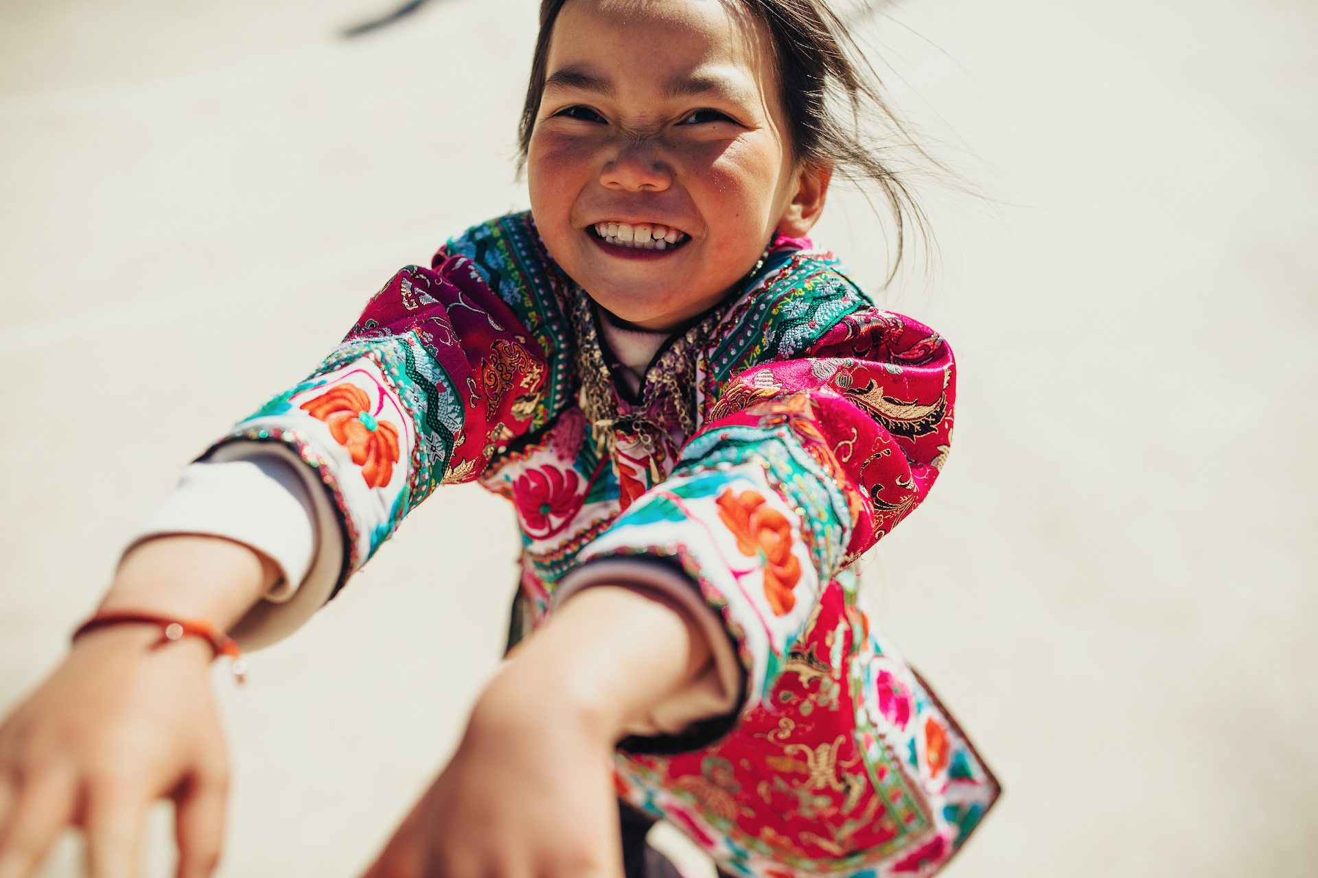 Girl from China in a colourful top smiles as she holds out her arms to the person holding the camera