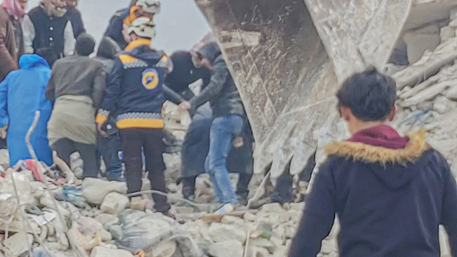 A boy with his back to the camera walks toward a group of people trying to rescue others from under rubble after the earthquake in Syria