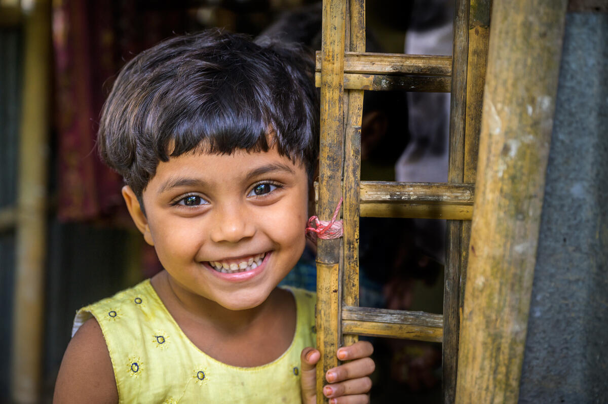 Sponsored child from Bangladesh smiles as she pokes her head around the side of a door