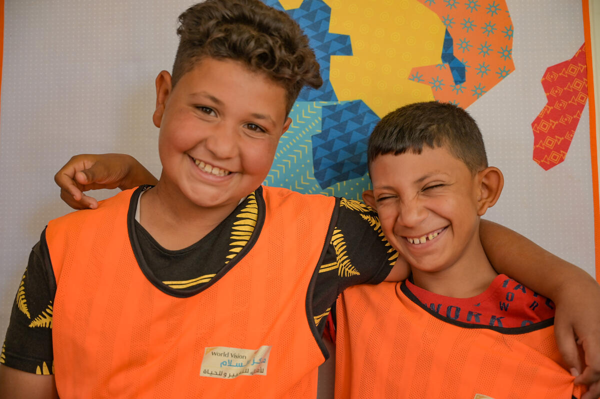 Two young boys wearing orange vests poses for a photo with their arms on their shoulders
