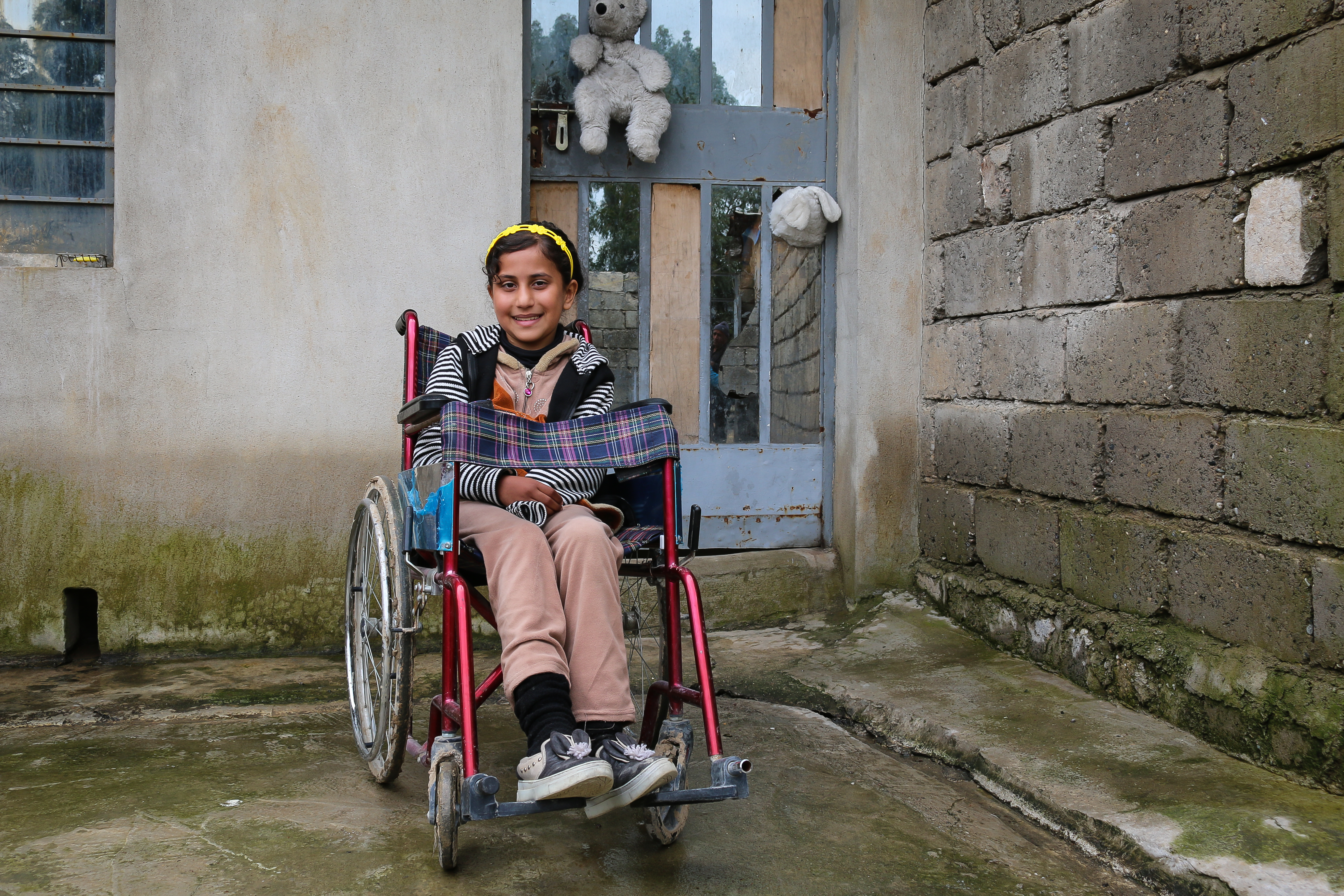 Girl from Iraq smiles as she sits outside in a wheelchair
