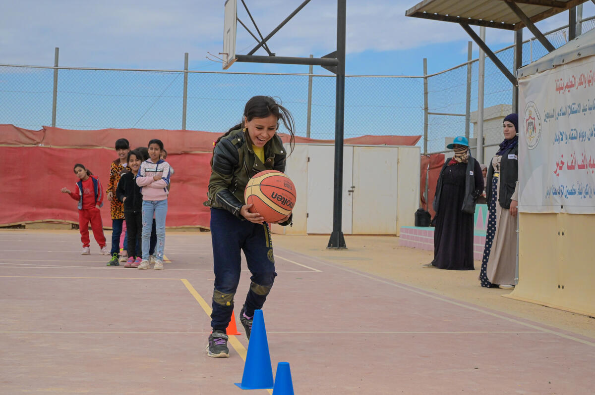 A Young girl holds a basketball while hopping over cones