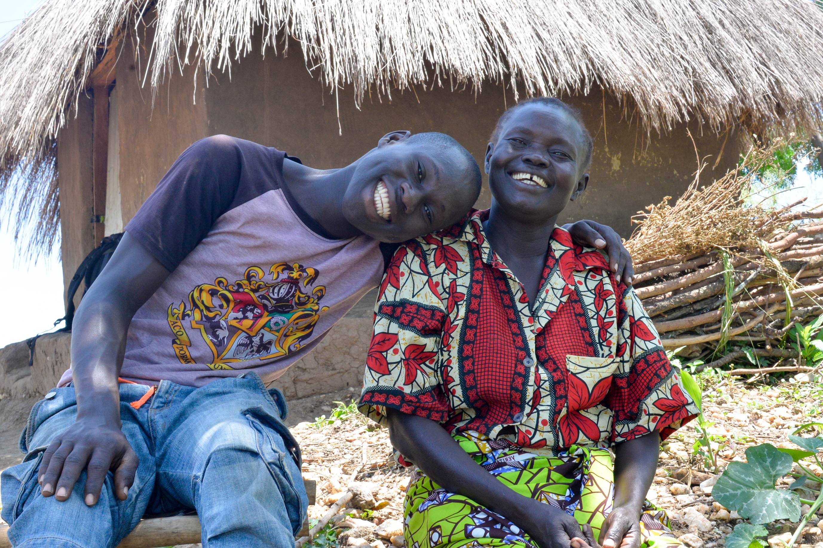 Joel a teenager from South Sudan, sat outside his new home in Uganda with his mum Margaret