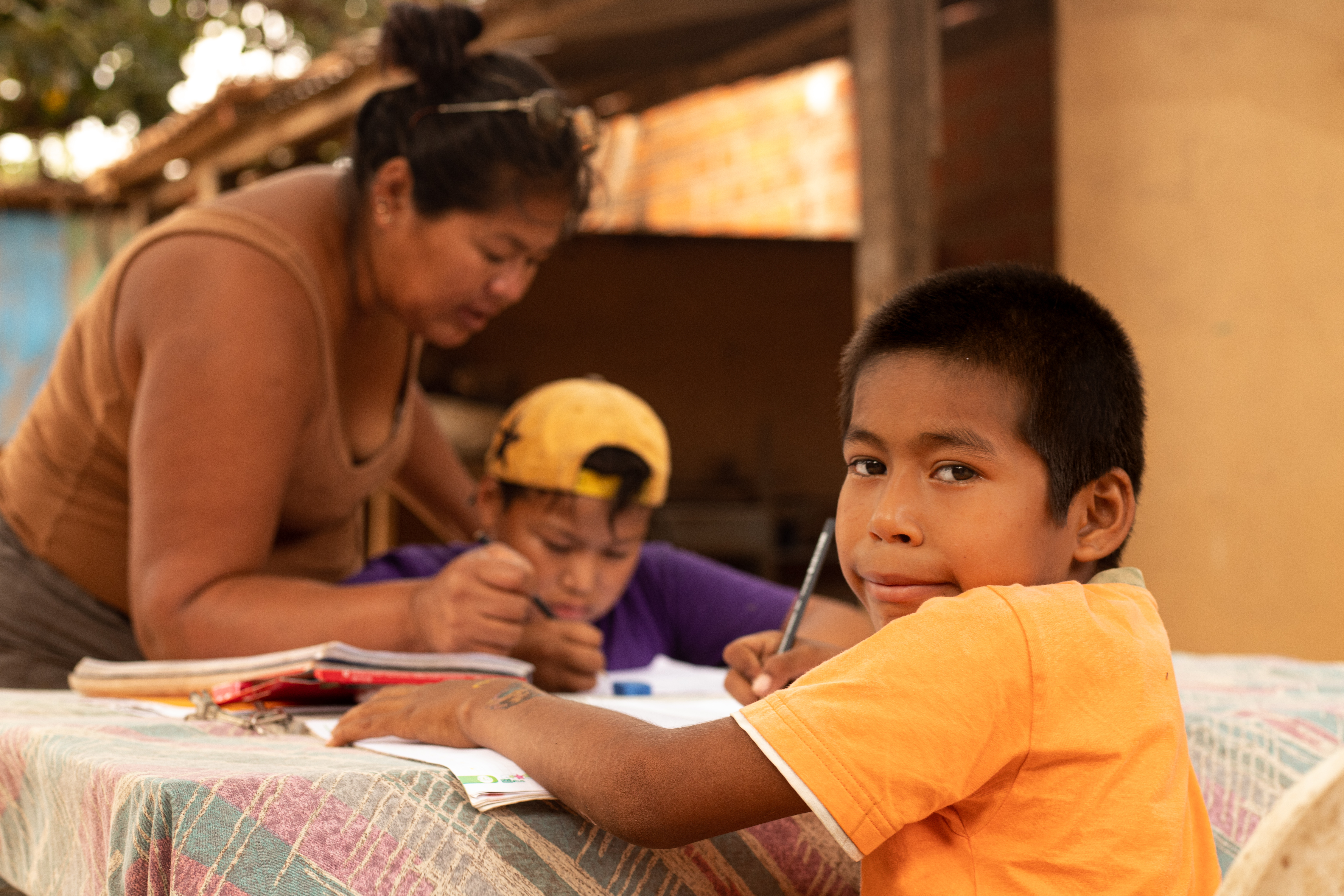 Boy in Bolivia does his school work on a table while his mother helps his brother to complete his, not allowing coronavirus to de-rail his education