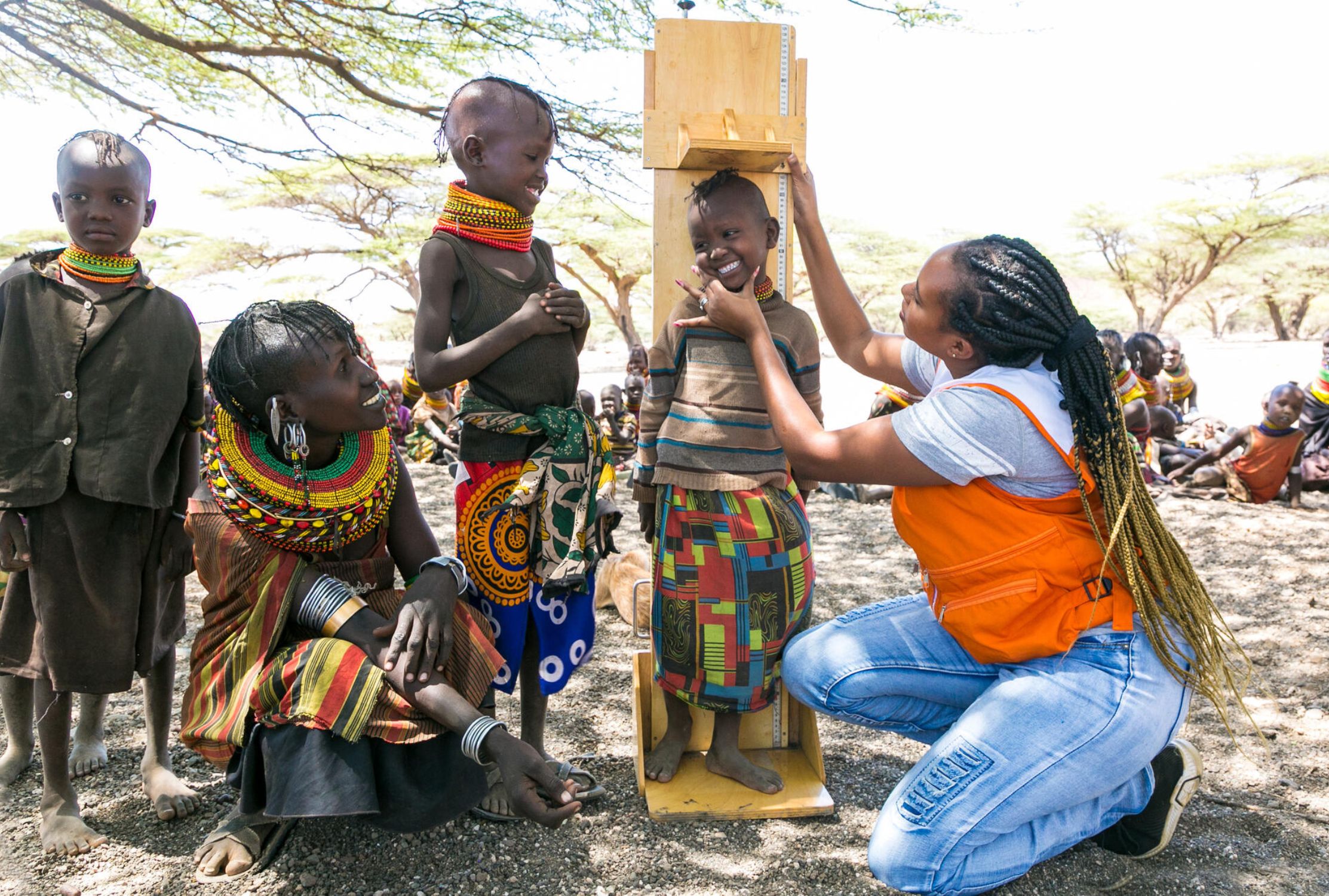 World Vision worker in an orange jacket measuring Kenyan children