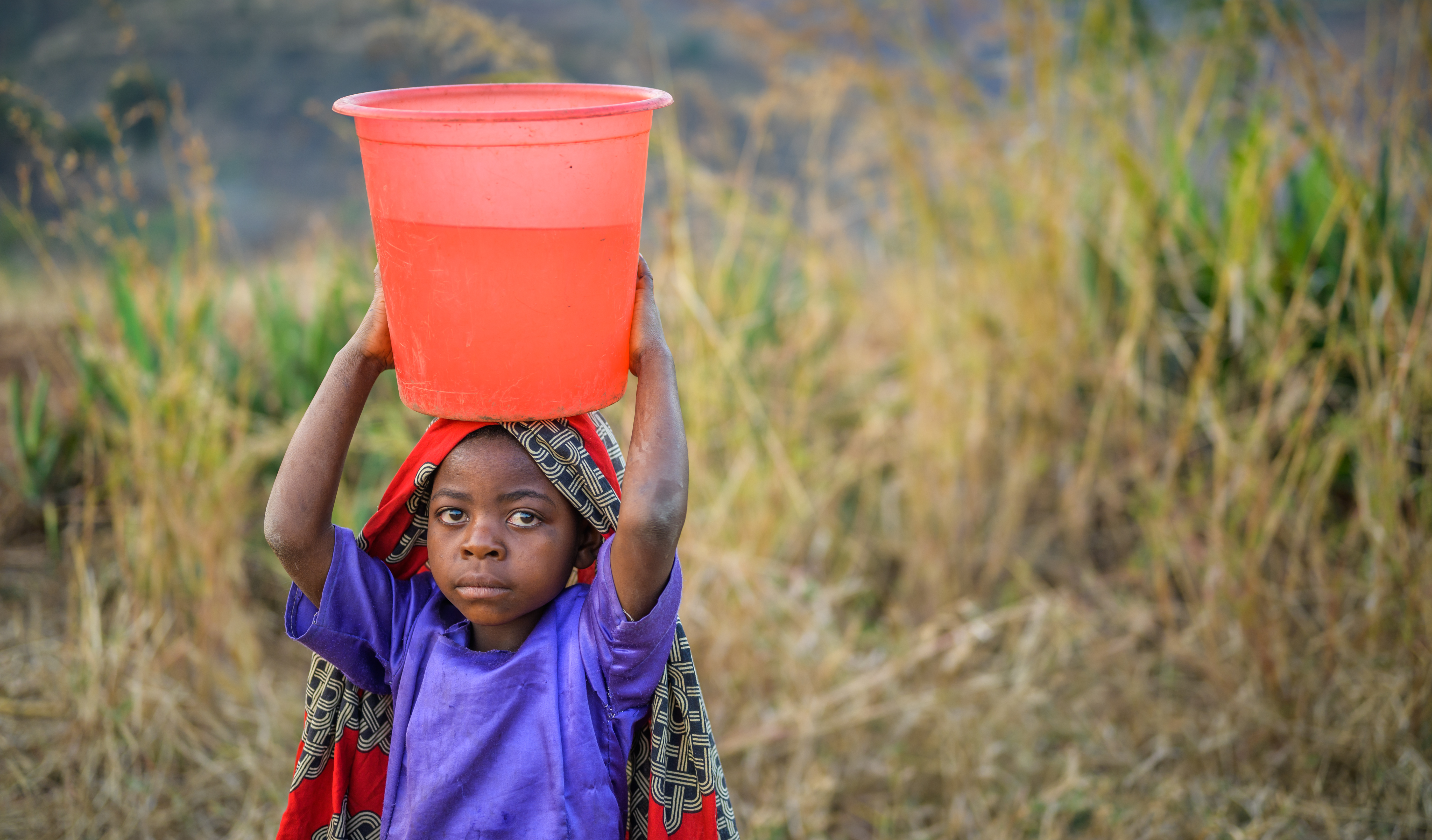 Child in Malawi walks holding a bucket of water over their head