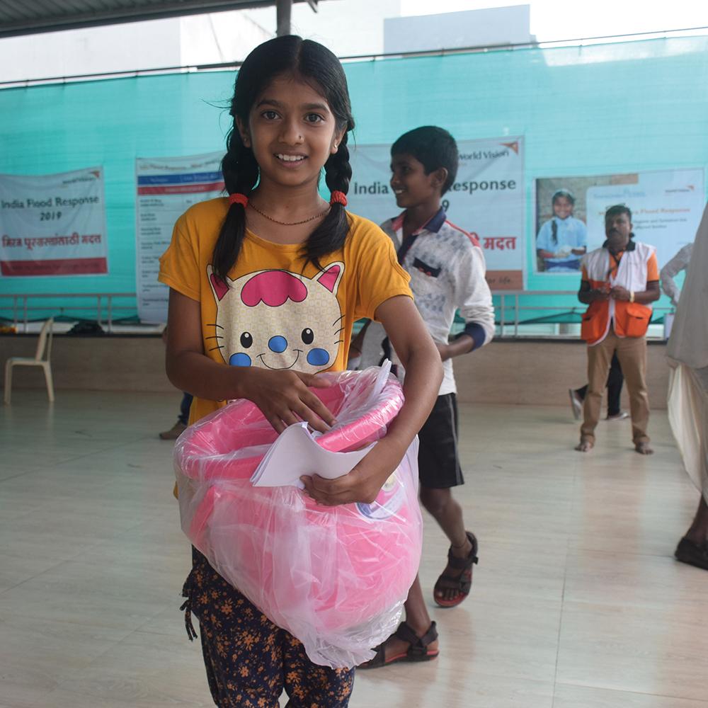 A girl from India holding a sanitary kit containing sanitary pads, underwear, water, and soap 