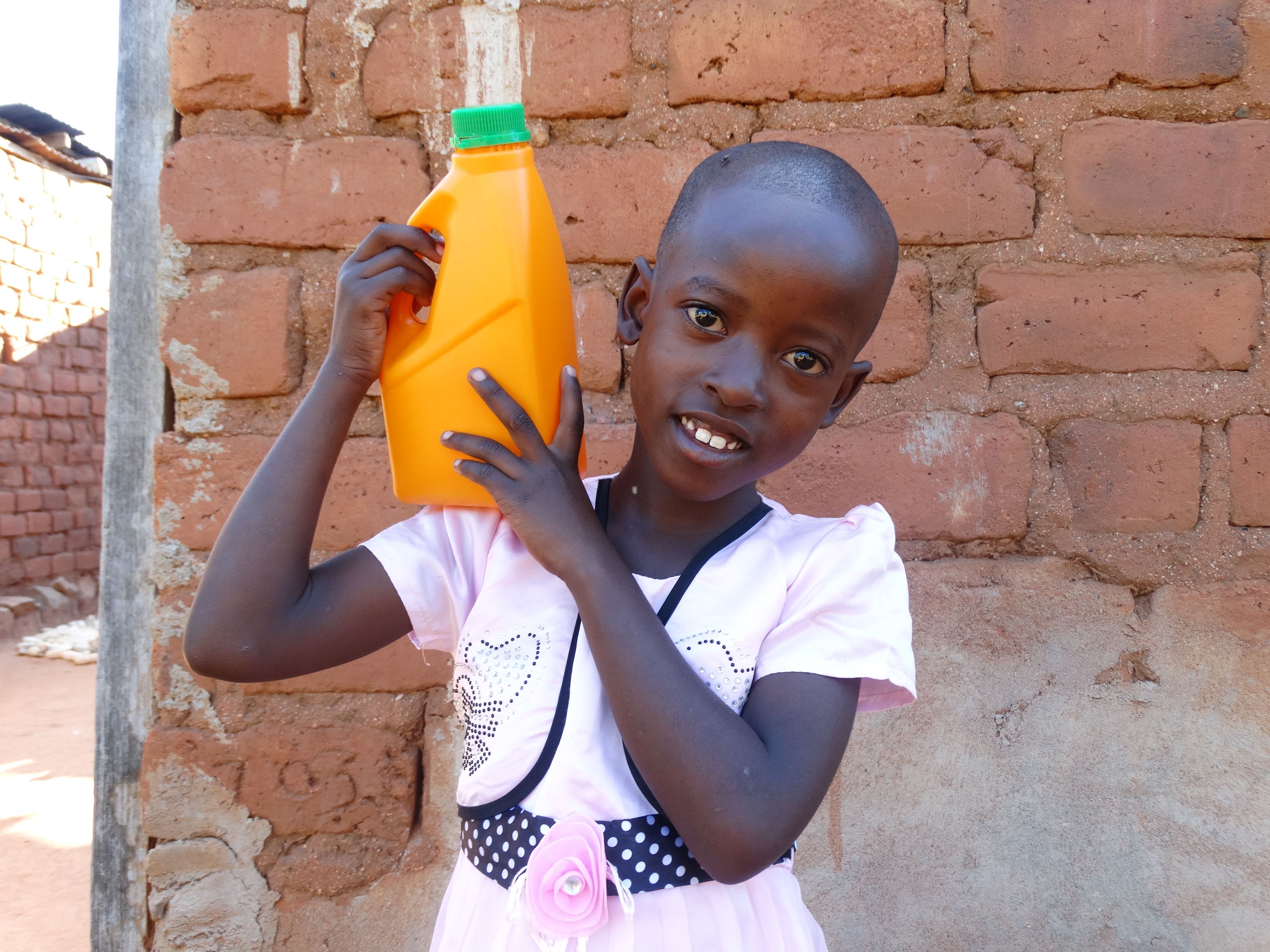 Girl from Tanzania smiles as she holds an orange jerrycan on her shoulder