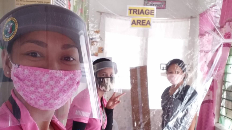 A health worker in the Philippines wears full protective gear to prevent the spread of COVID-19, with her colleagues in the background