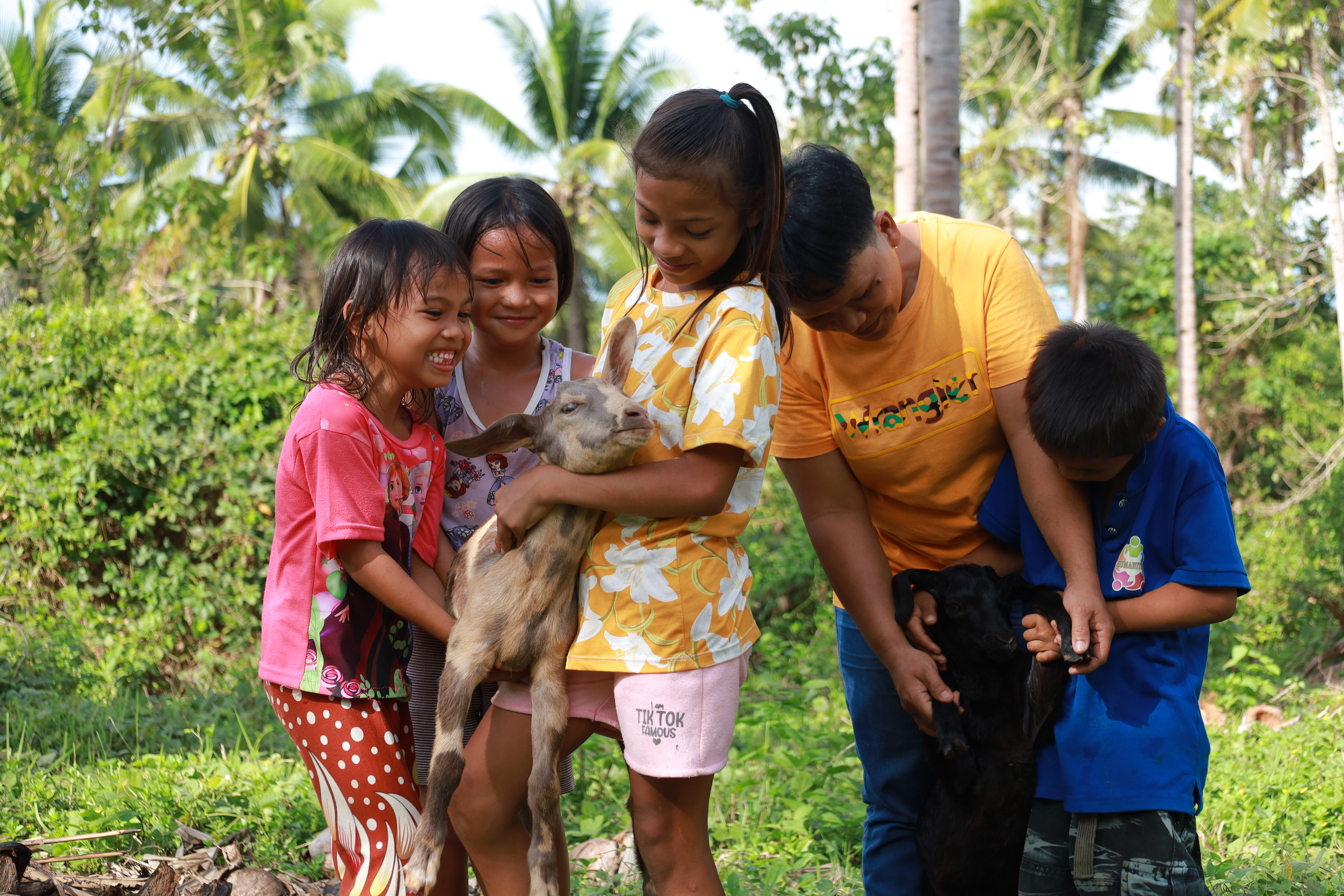 Five children smiling whilst playing with and holding up their goats.