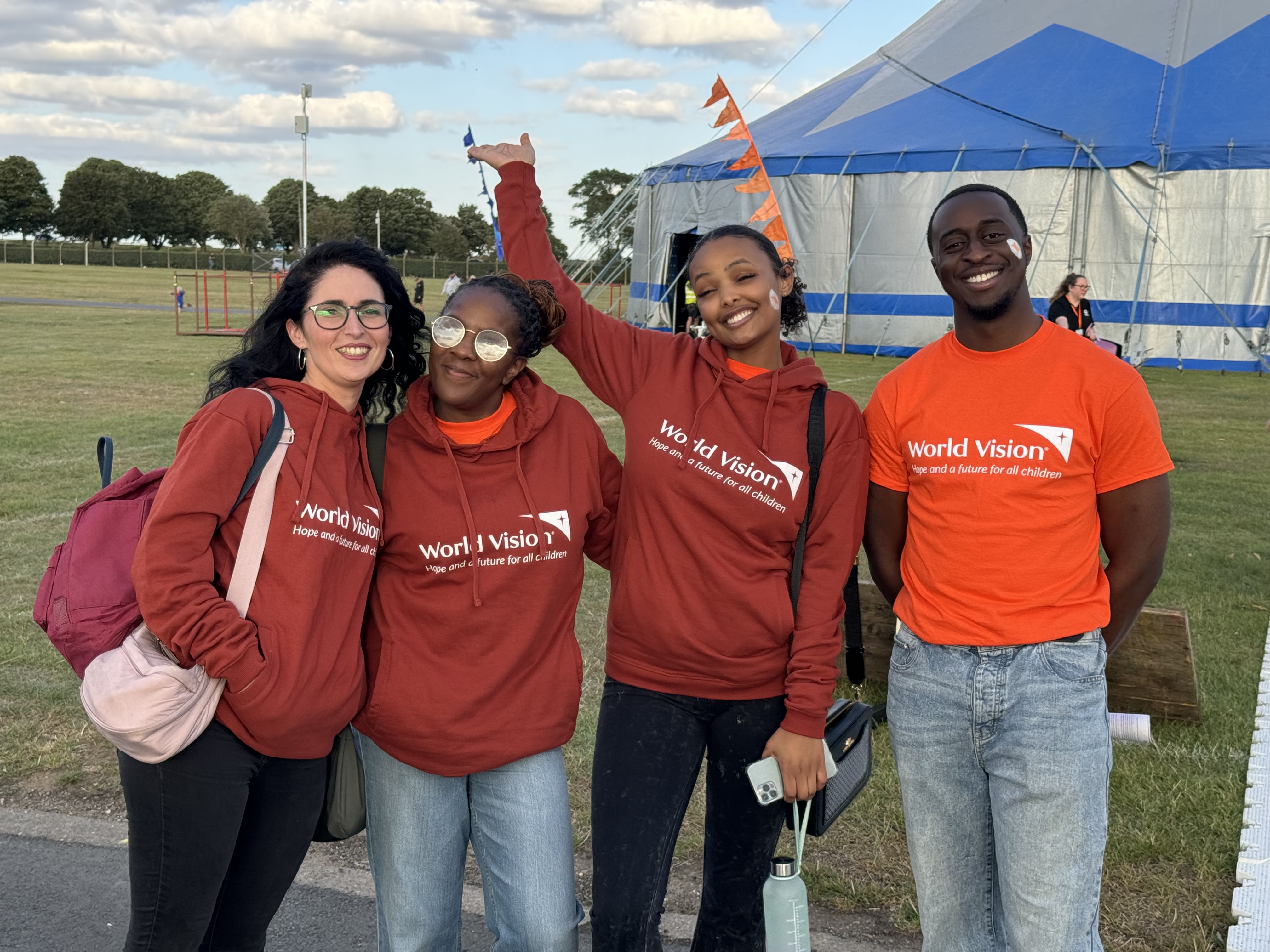 Four World Vision branded volunteers smiling at a festival in front of big tent