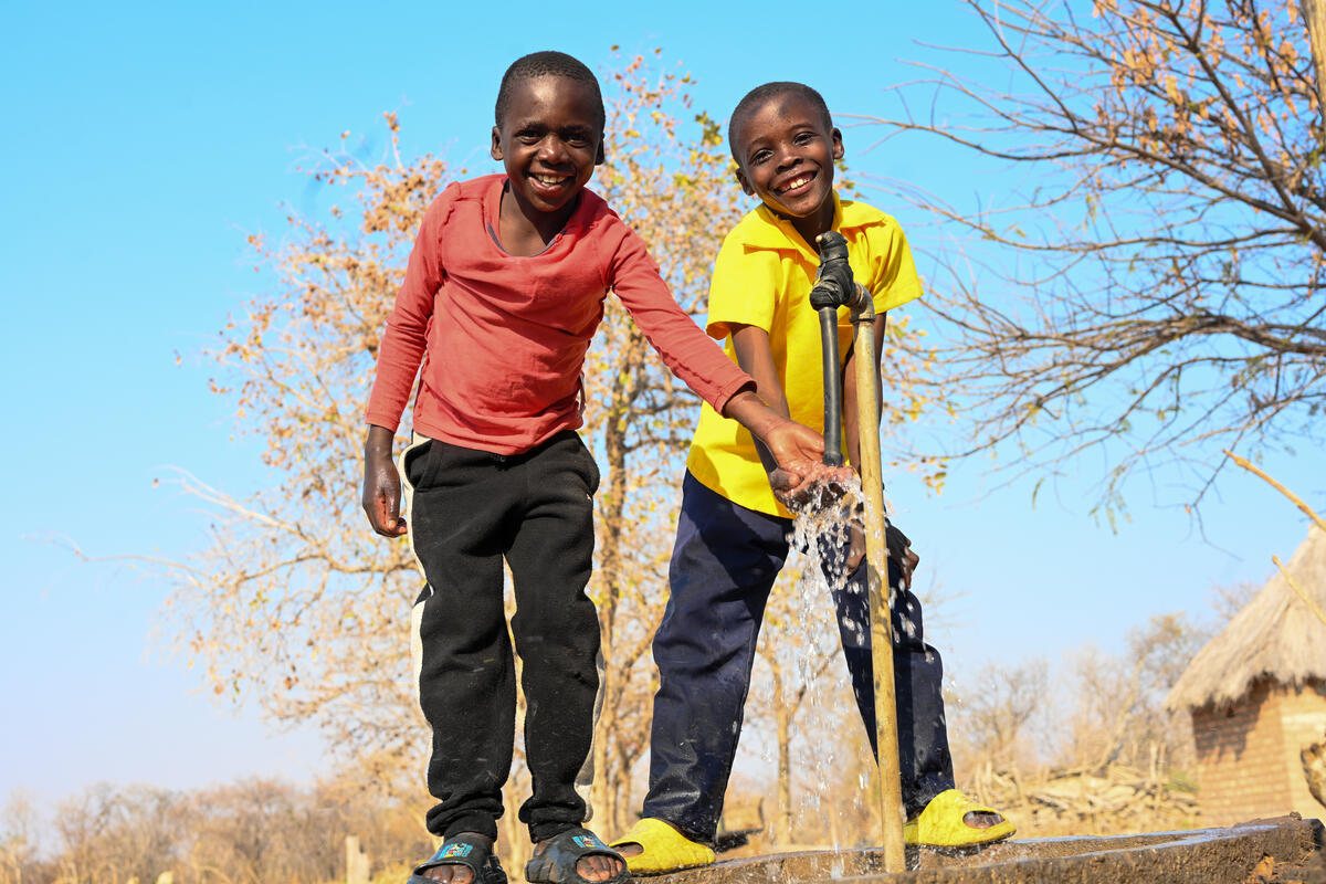 Two children smiling and playing by a fresh water tap