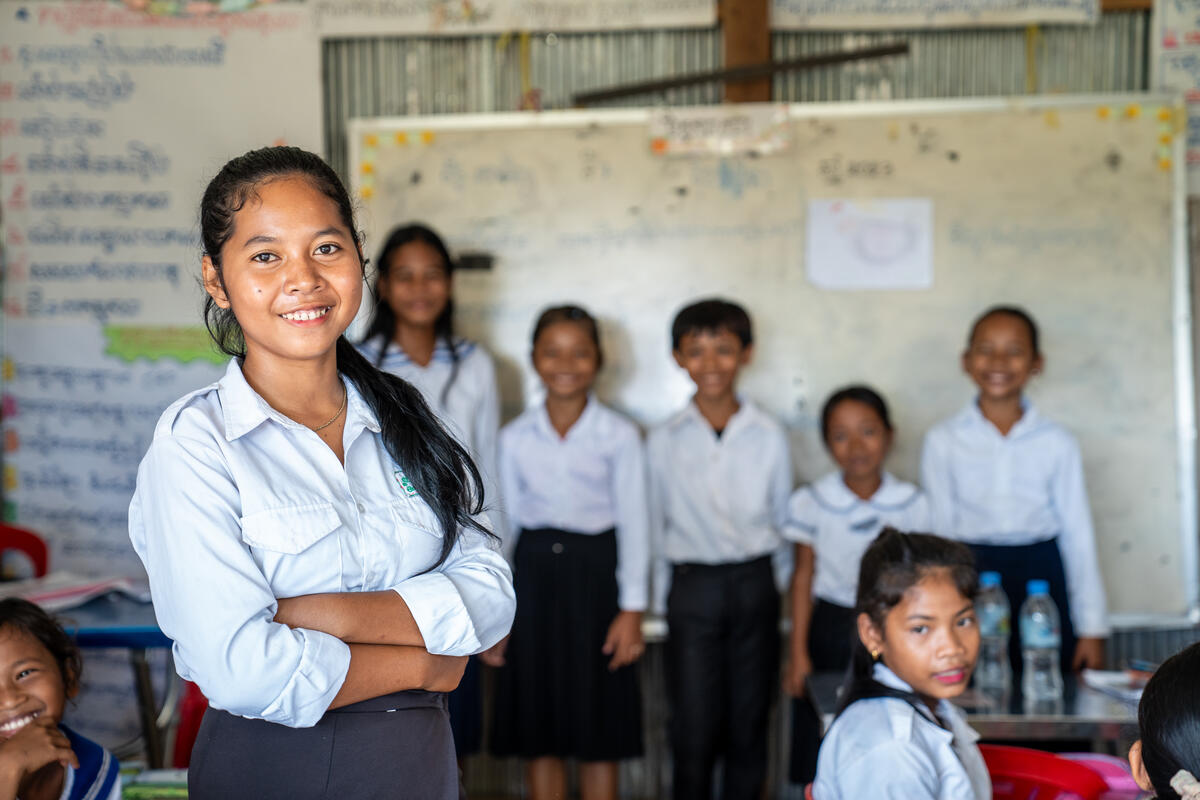 A girl stands with arms crossed and smiling in front of classmates
