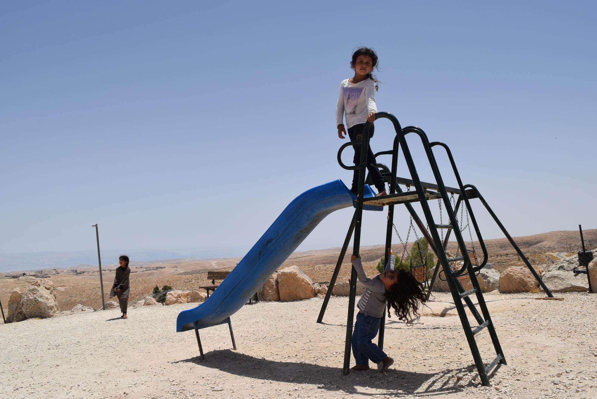 Two young girls play on a slide in West Bank