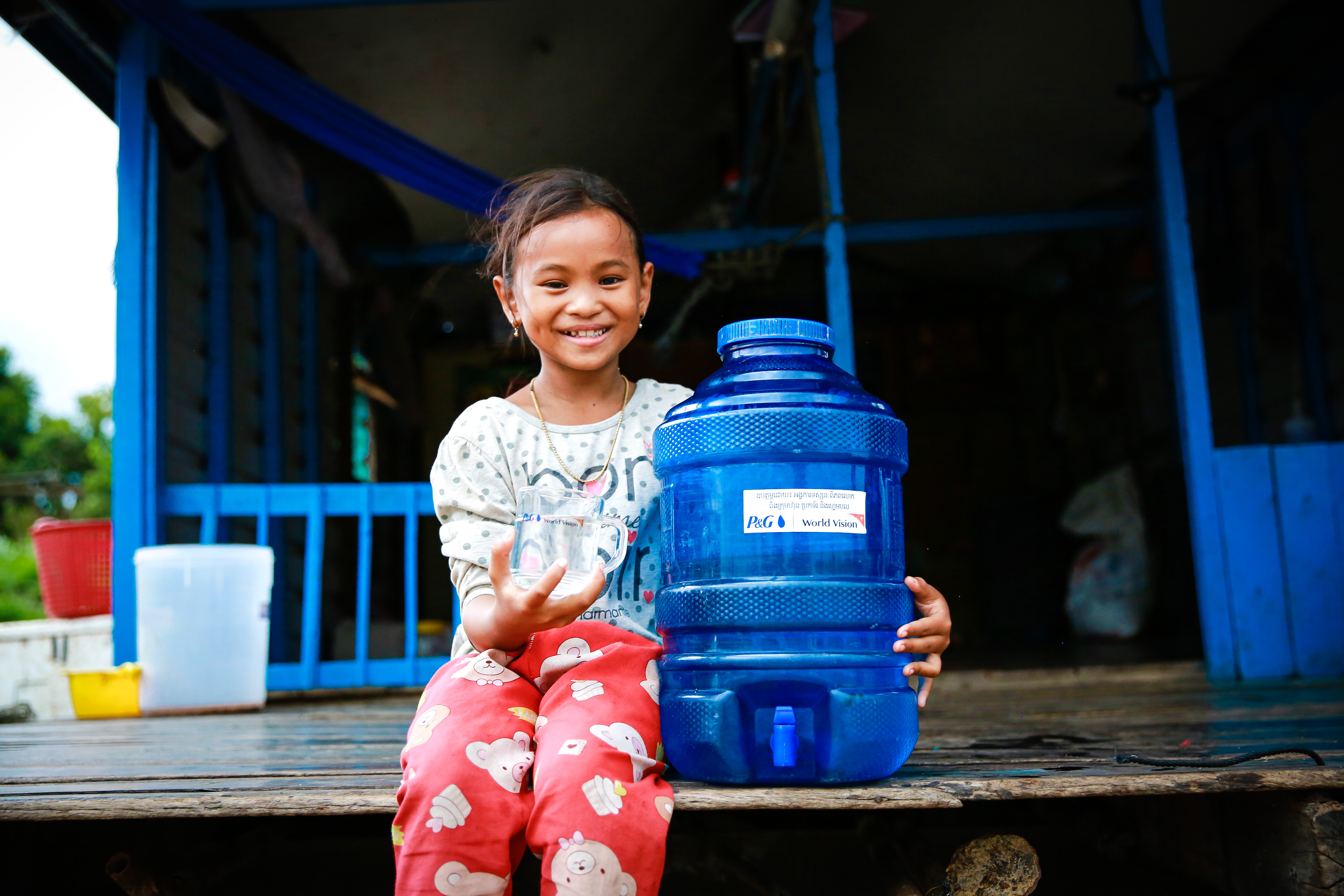 A girl in Cambodia smiles to camera whilst holding a container of clean water