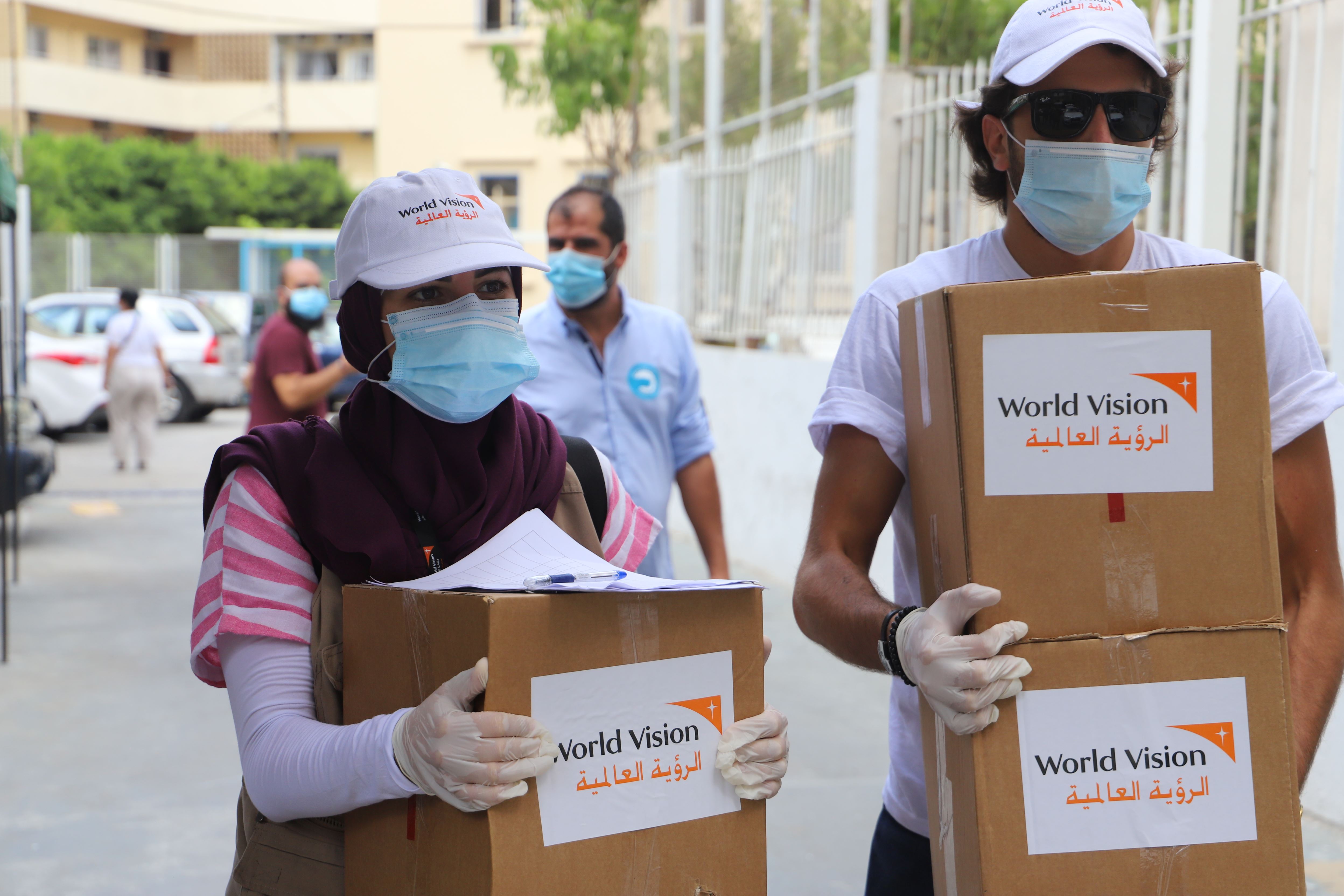 Staff members in masks and gloves carry boxes to distribute mini food kits