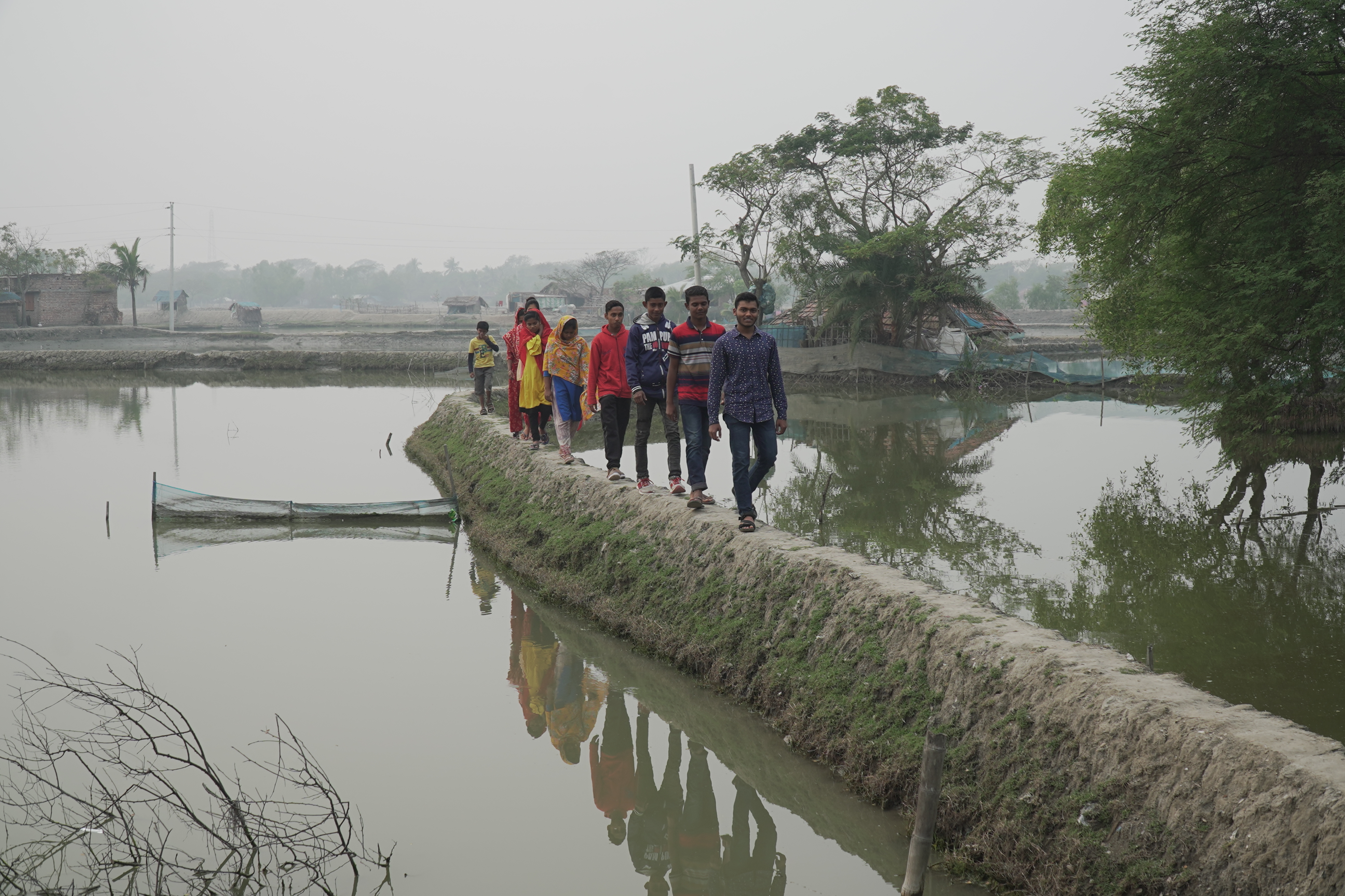 People walk along a wall in Bangladesh, next to a flood that disrupted their village
