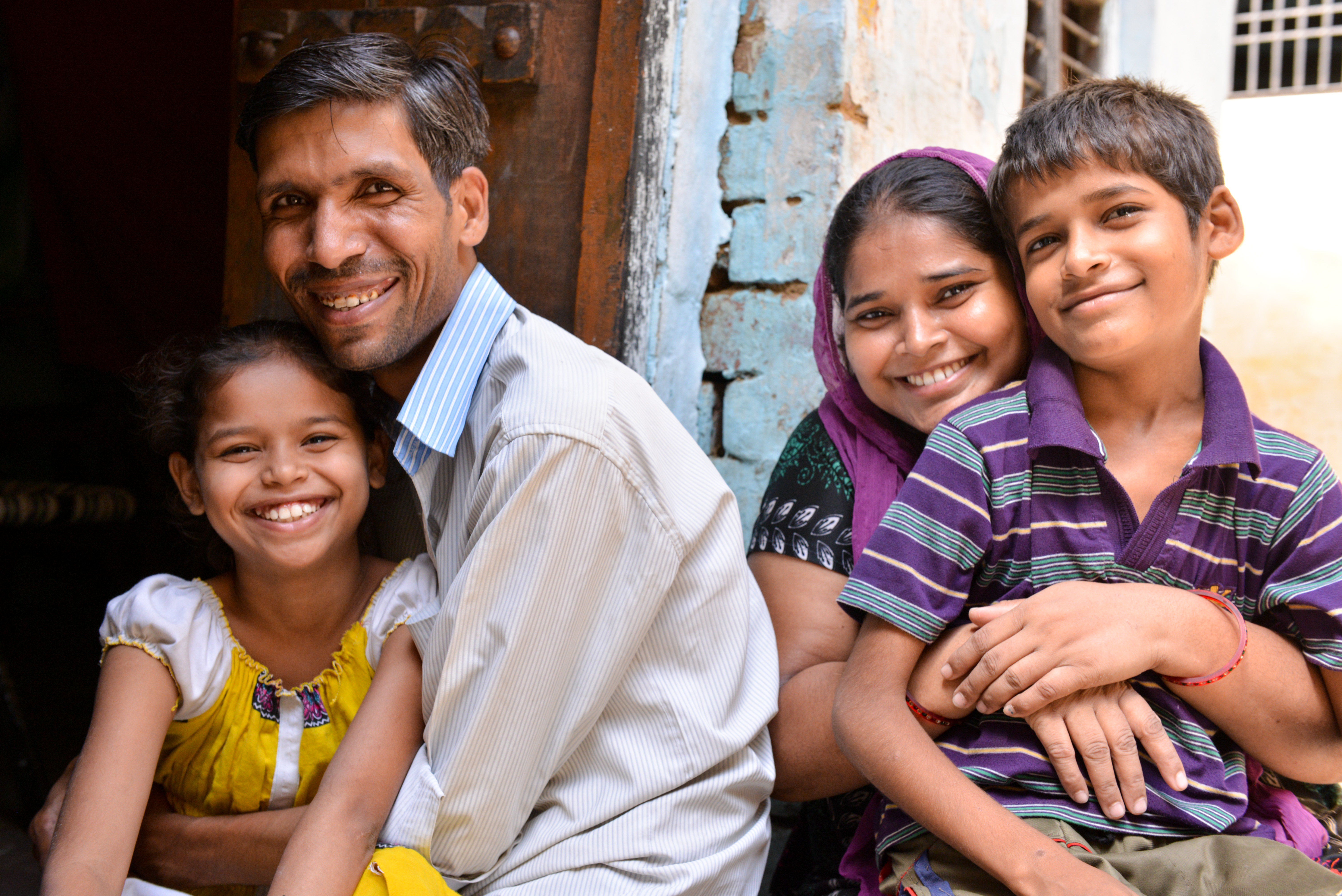 Smiling man and woman hug their grinning children outside building in India