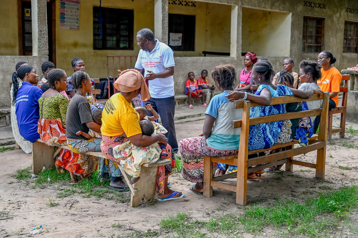 Community in DRC sit together with World Vision worker