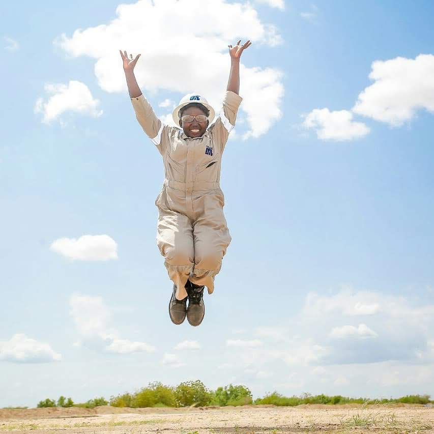 Pauline, wearing hard hat and overalls, jumps for joy 