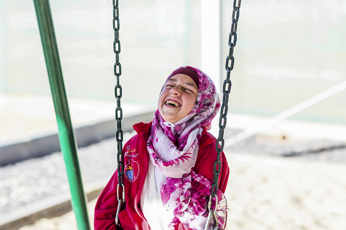 Syrian refugee smiles and tilts her head back as she sits on a swing in Jordan
