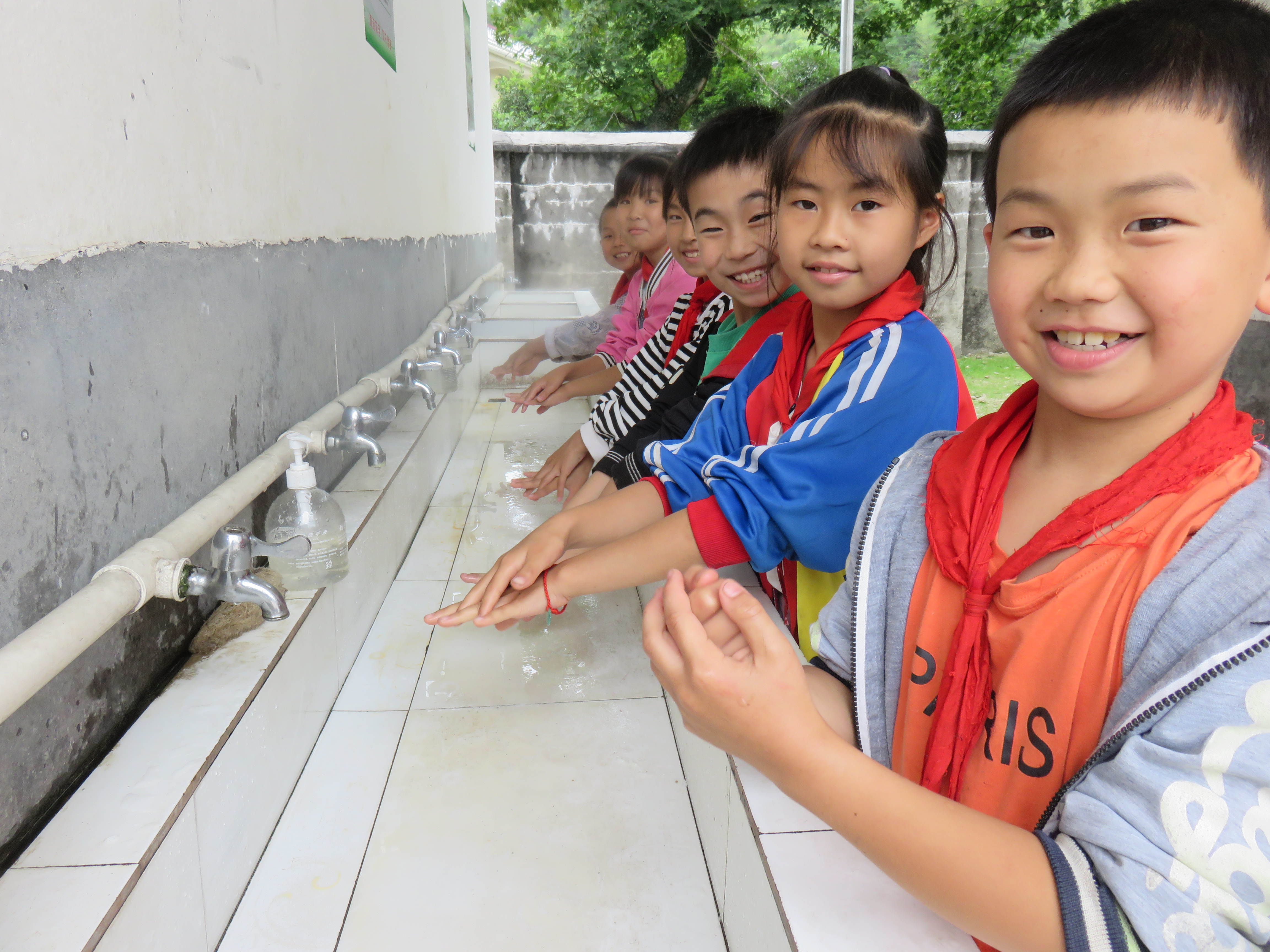Children in China smile as they demonstrate their hand washing technique in front of sinks