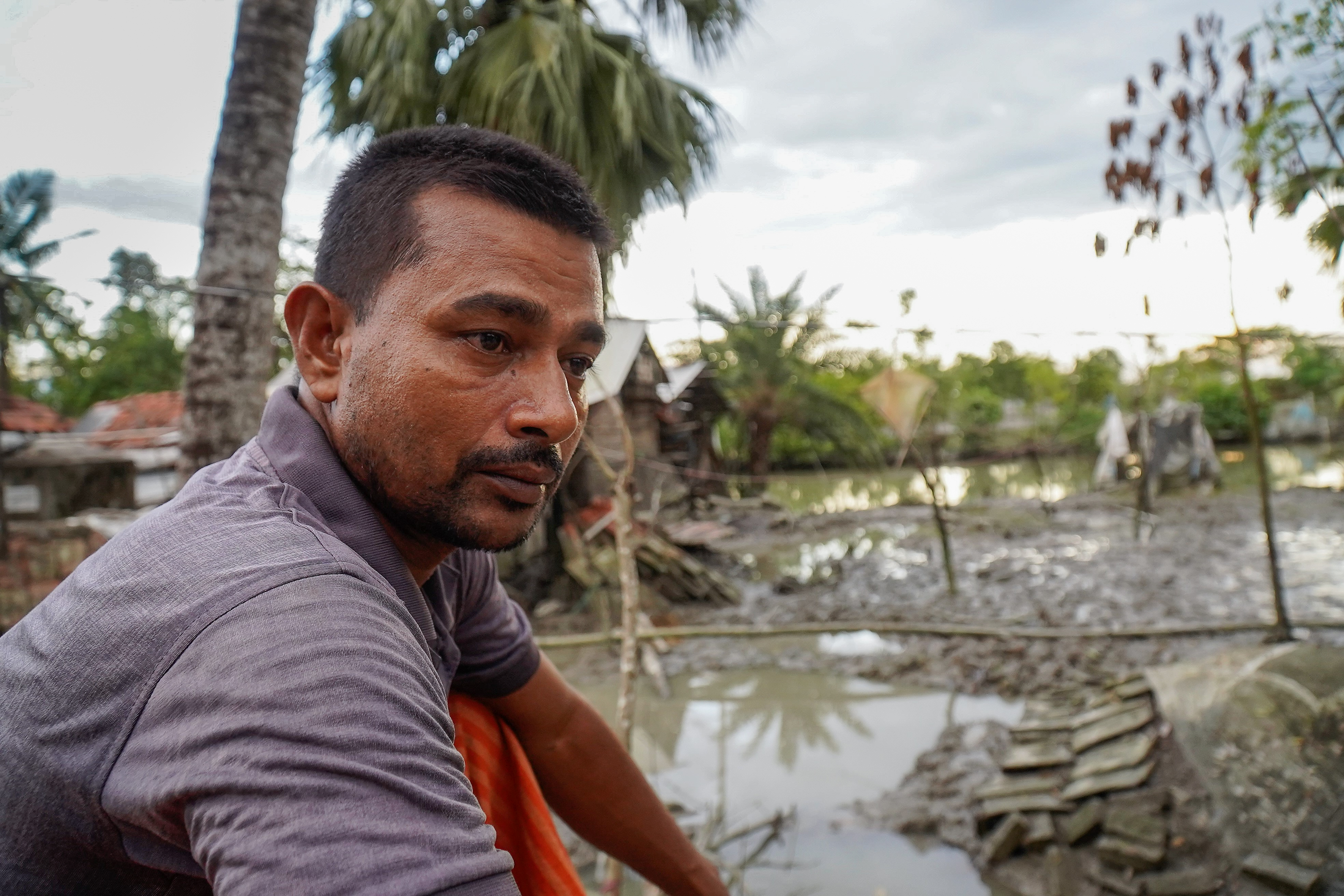 Man in Bangladesh looks into the camera, sitting next to a flood that destroyed his shrimp farm