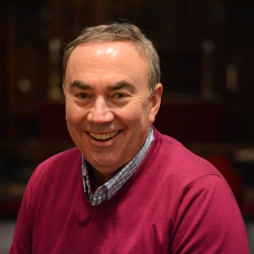 Man in the UK smiles into the camera wearing a shirt and cardigan